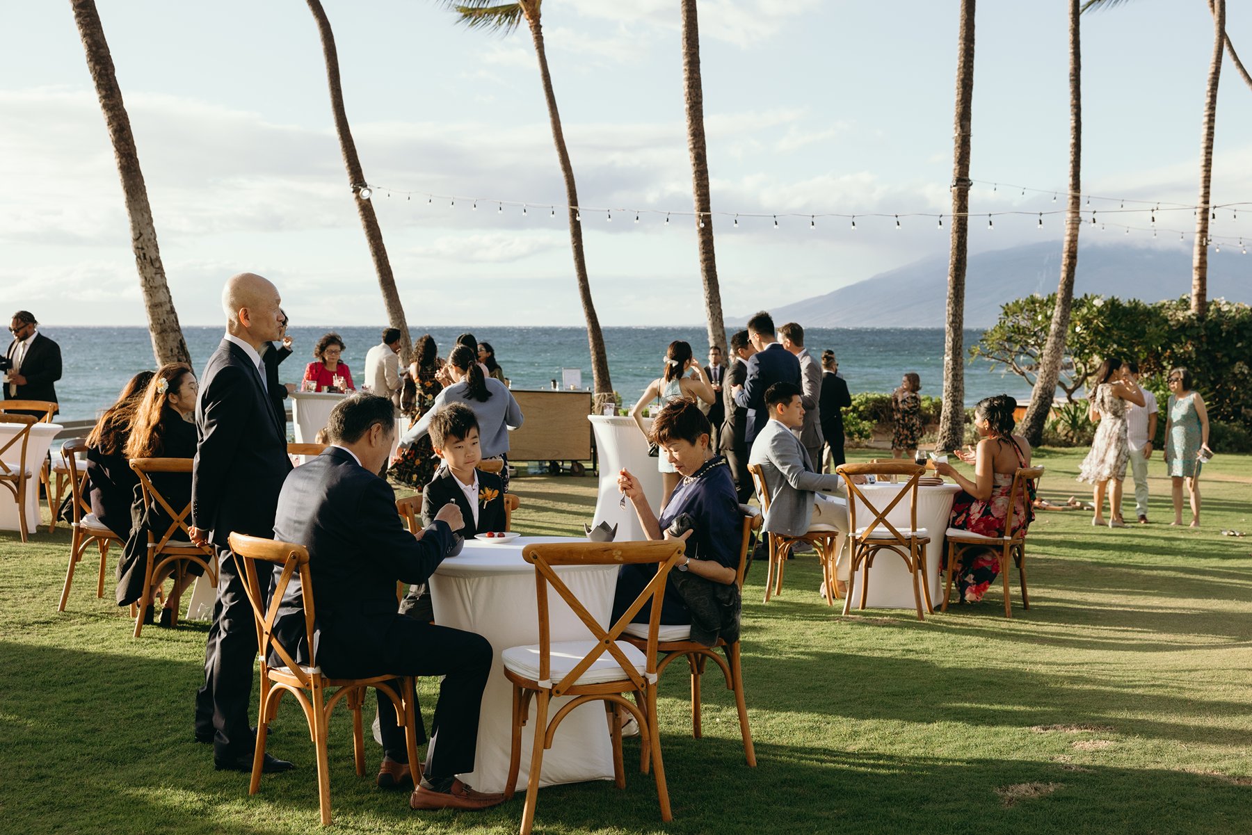 Guests seated and mingling at outdoor reception overlooking ocean at Hawaii resort wedding venue