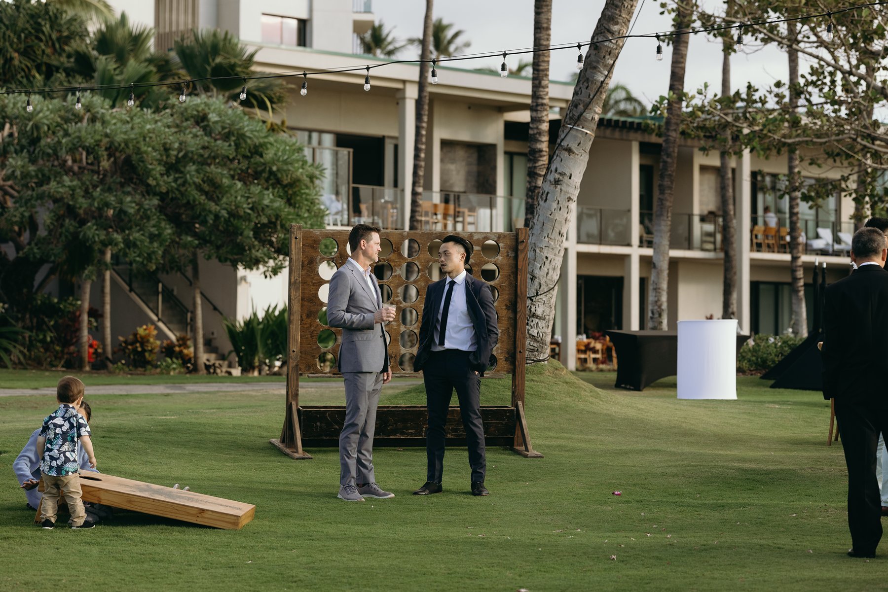 Guests mingling and playing lawn games outside modern Hawaii resort wedding venue