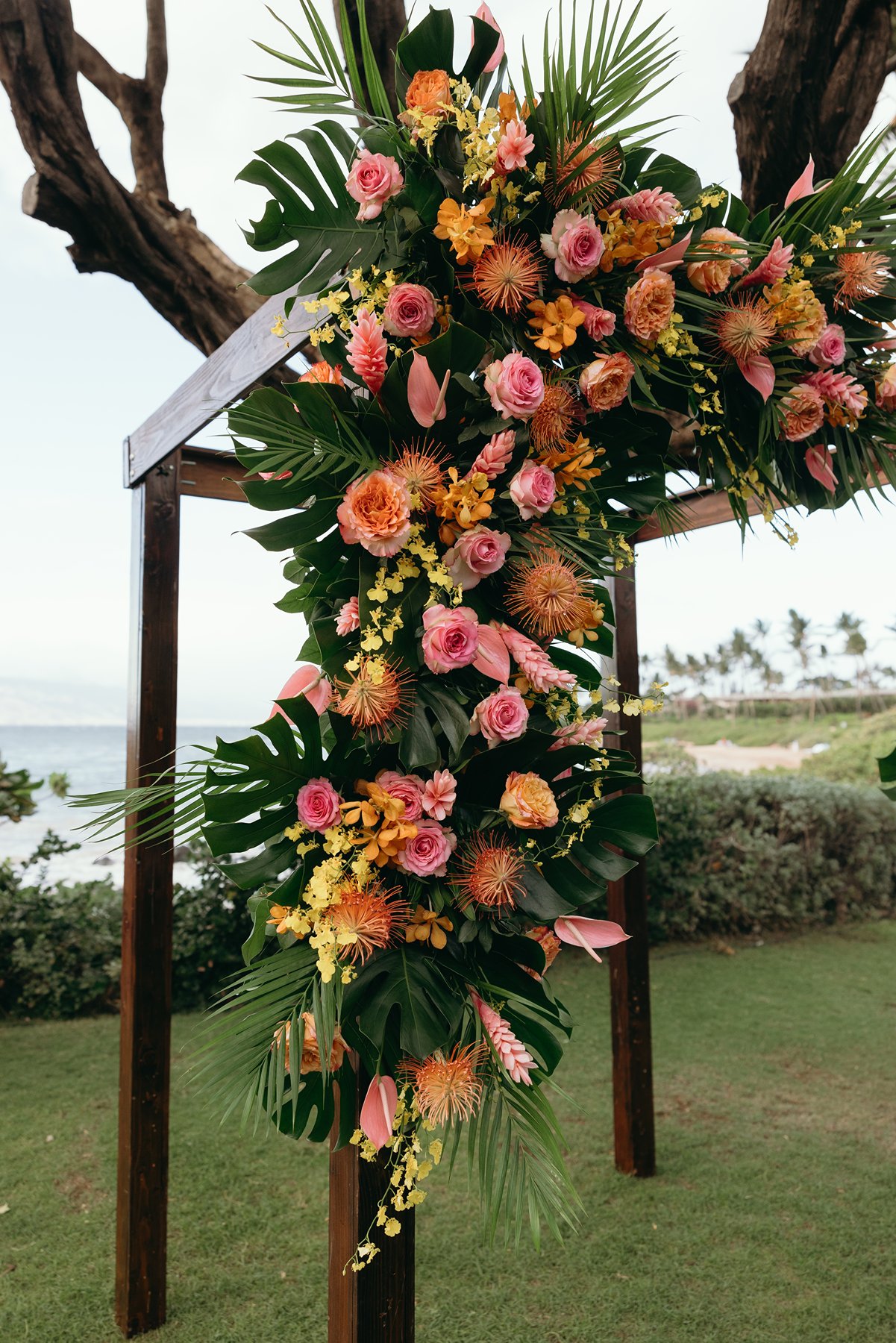 Tropical floral ceremony arch with pink and orange flowers at Maui wedding venue