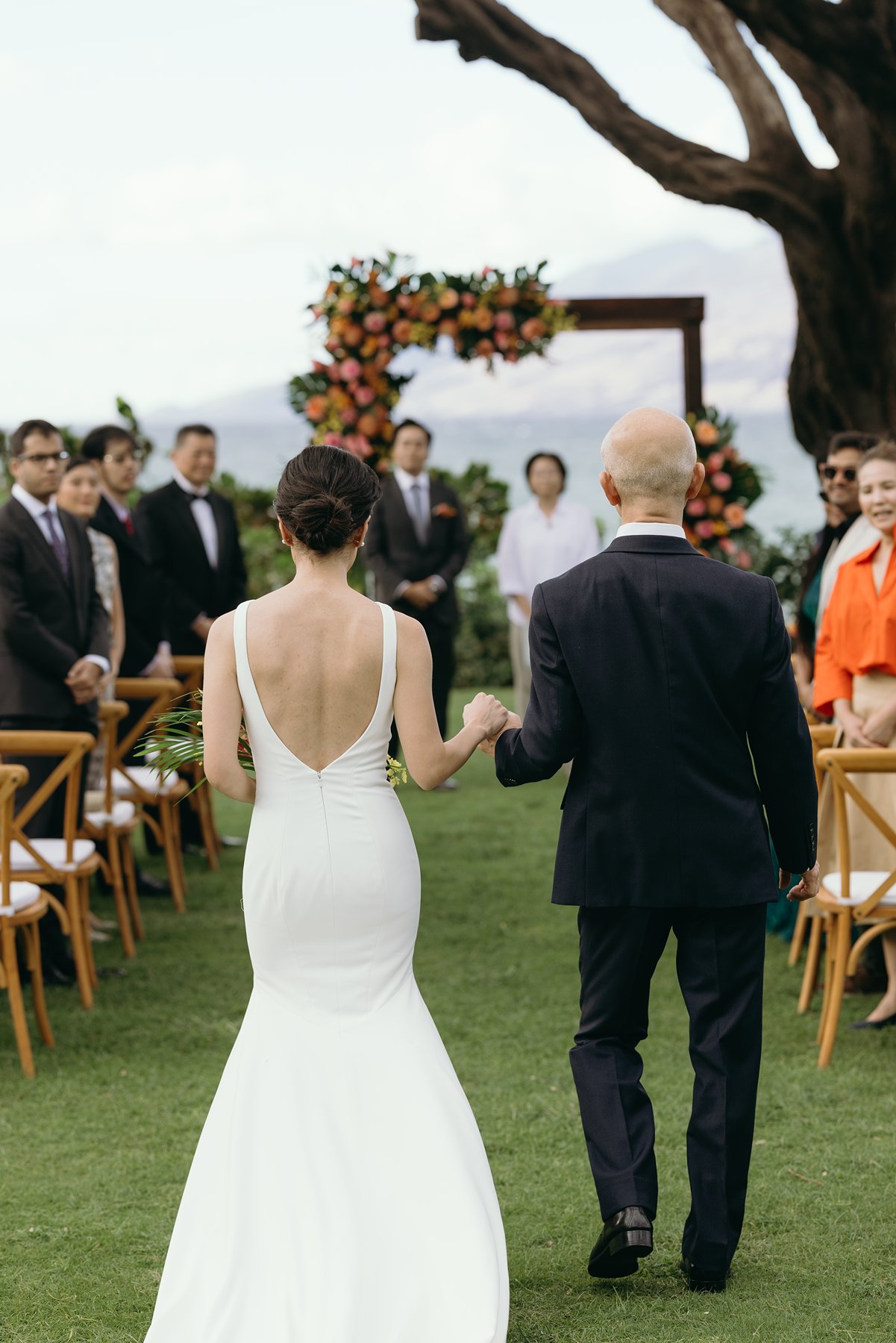 Bride walking down aisle holding bouquet during outdoor Hawaii wedding ceremony