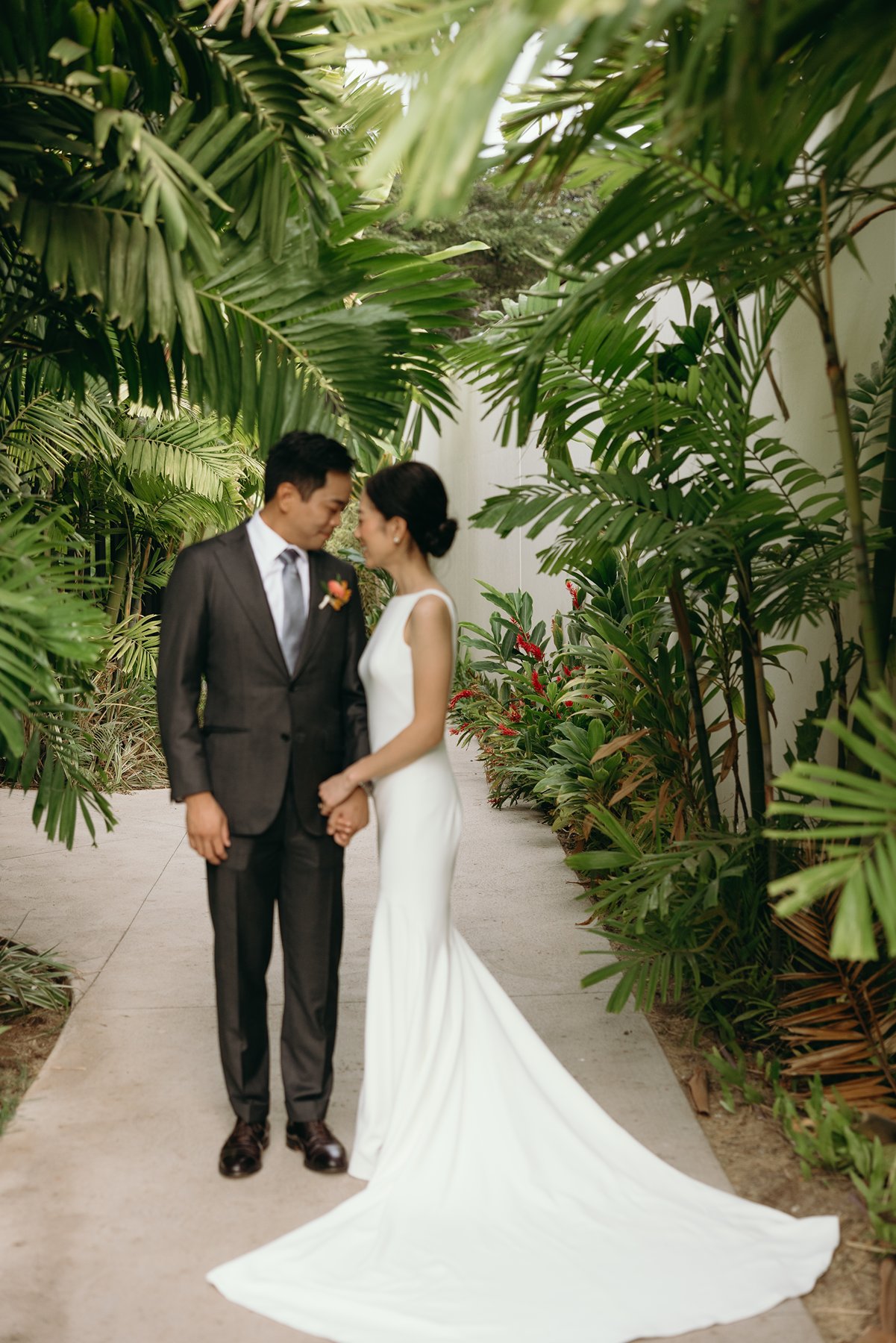 Bride and groom standing together in lush tropical garden pathway at Maui resort wedding venue
