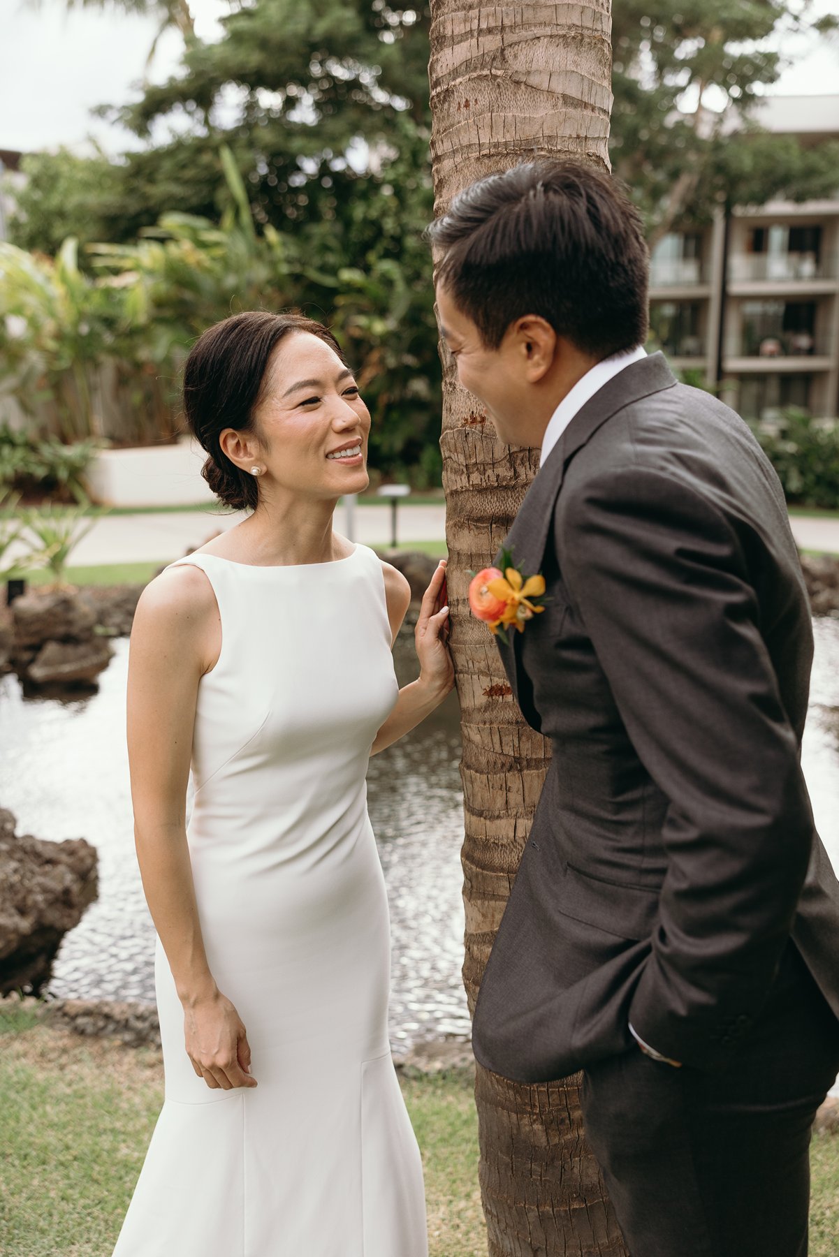 Bride and groom sharing a moment by palm tree near water feature at Hawaii wedding venue