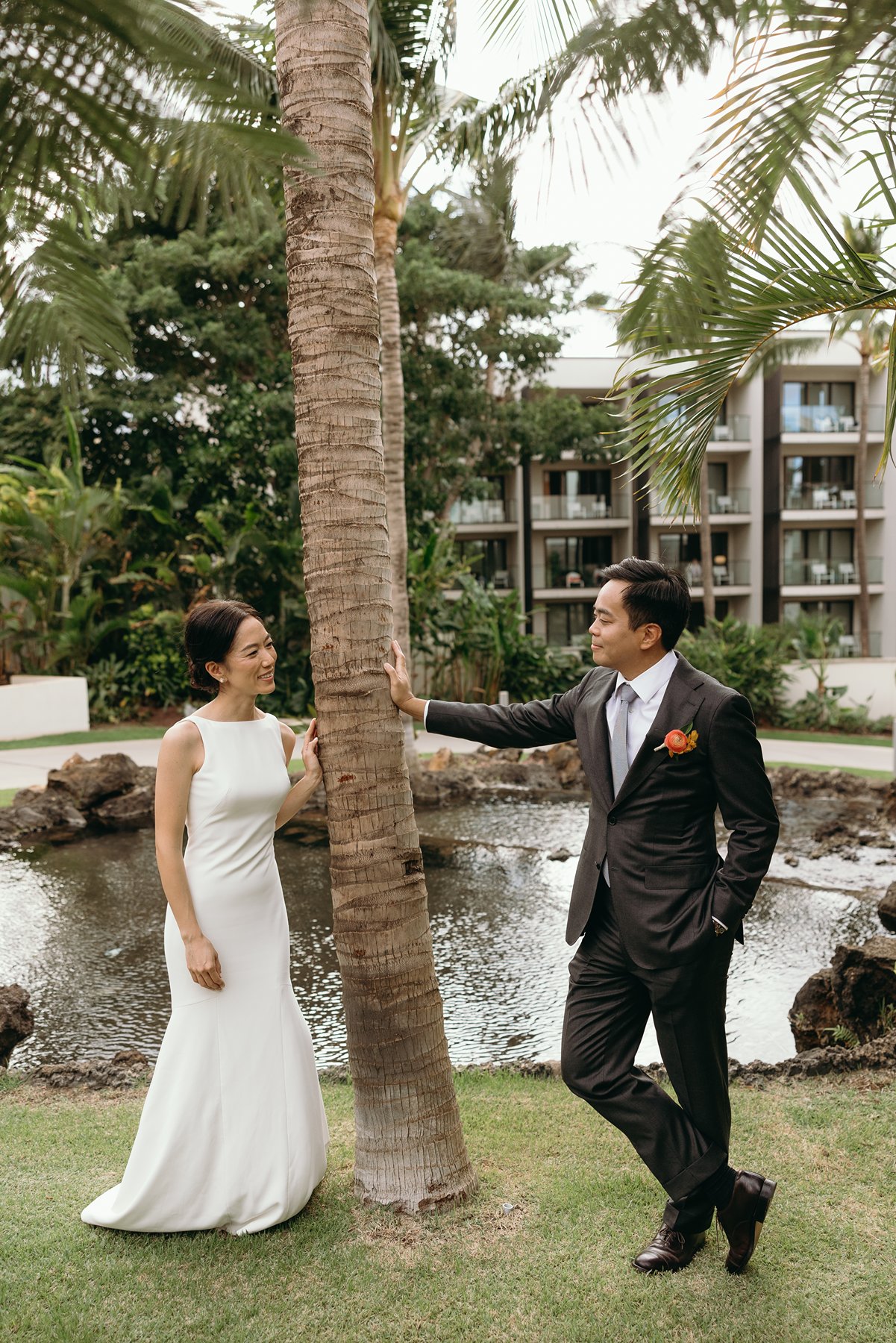Bride and groom standing by palm tree near water feature at Hawaii resort wedding venue