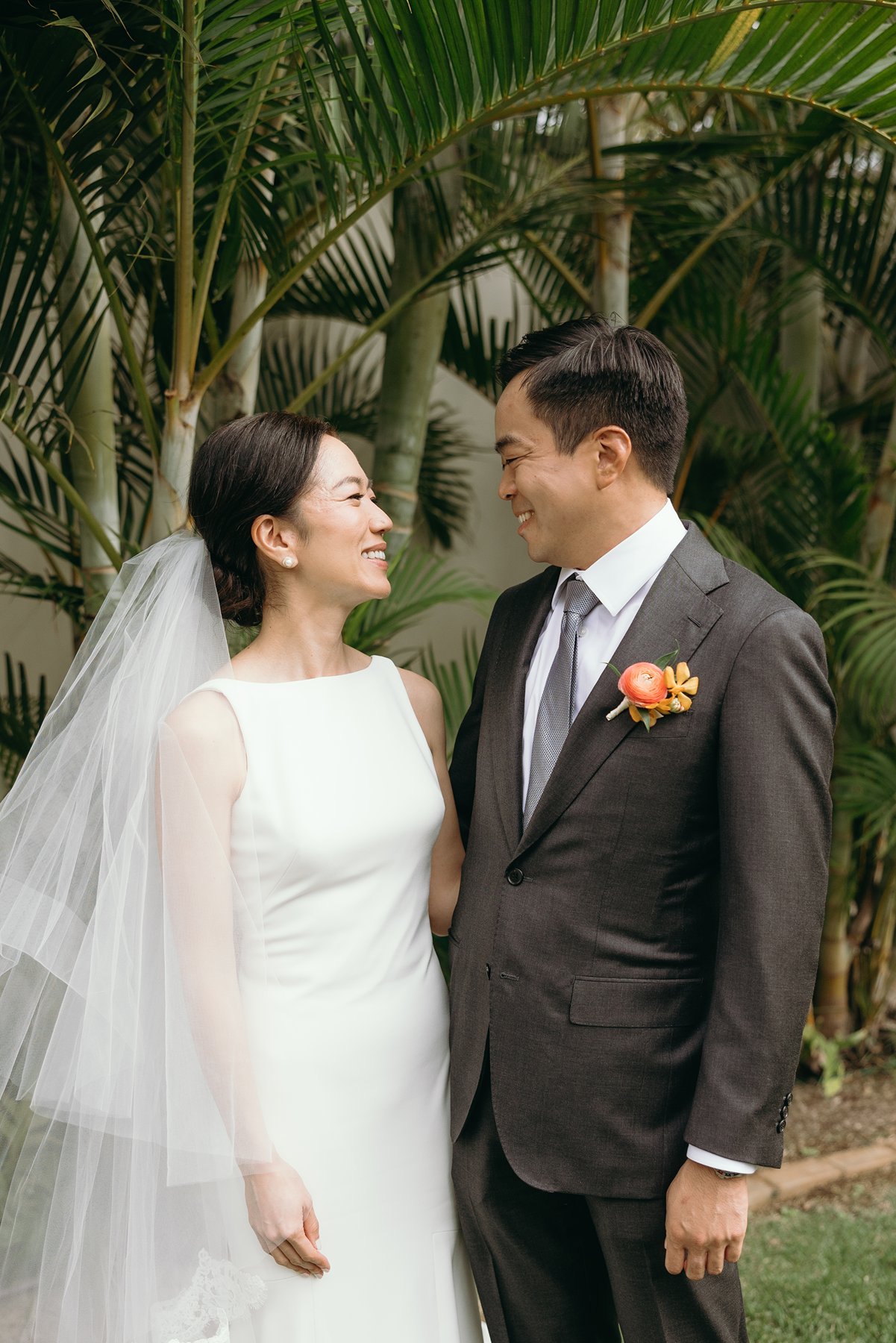Close-up of bride and groom smiling at each other surrounded by tropical greenery