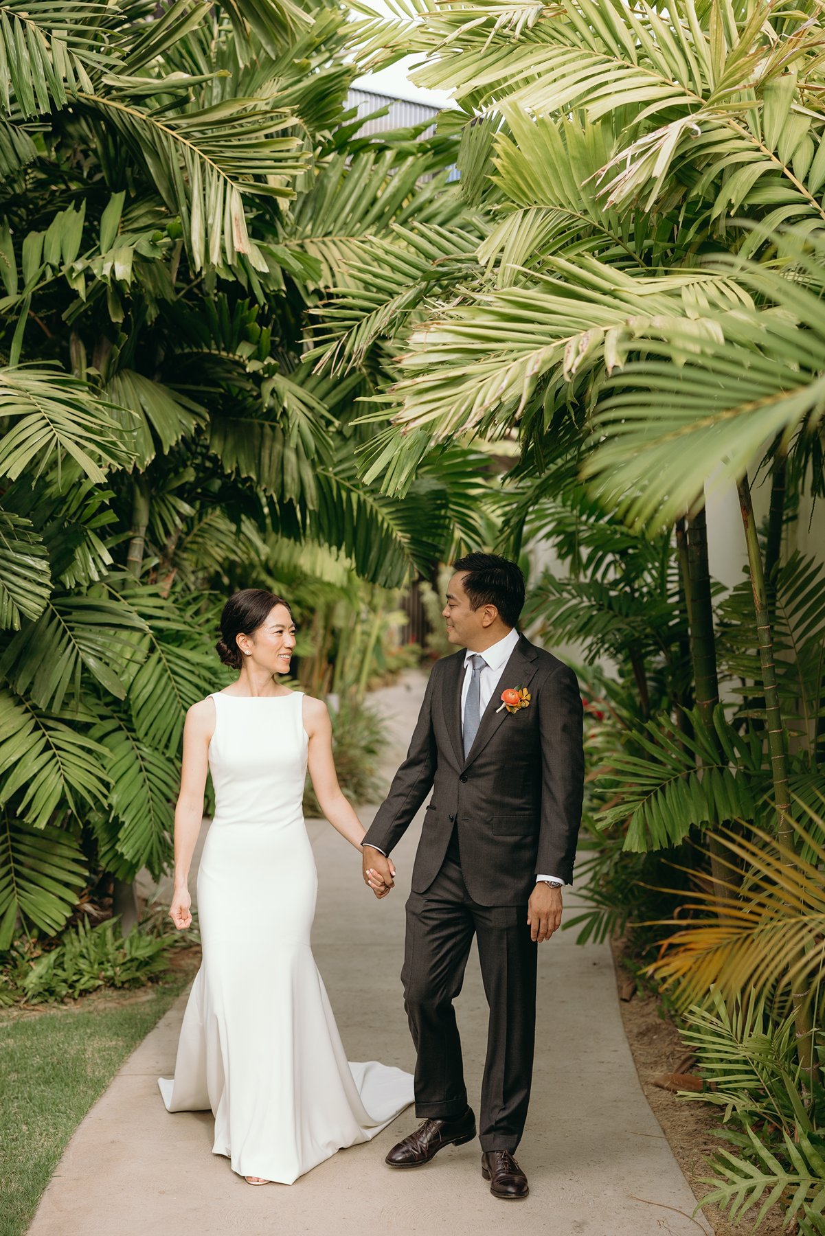 Bride and groom walking hand in hand through palm-lined path at Maui resort wedding venue