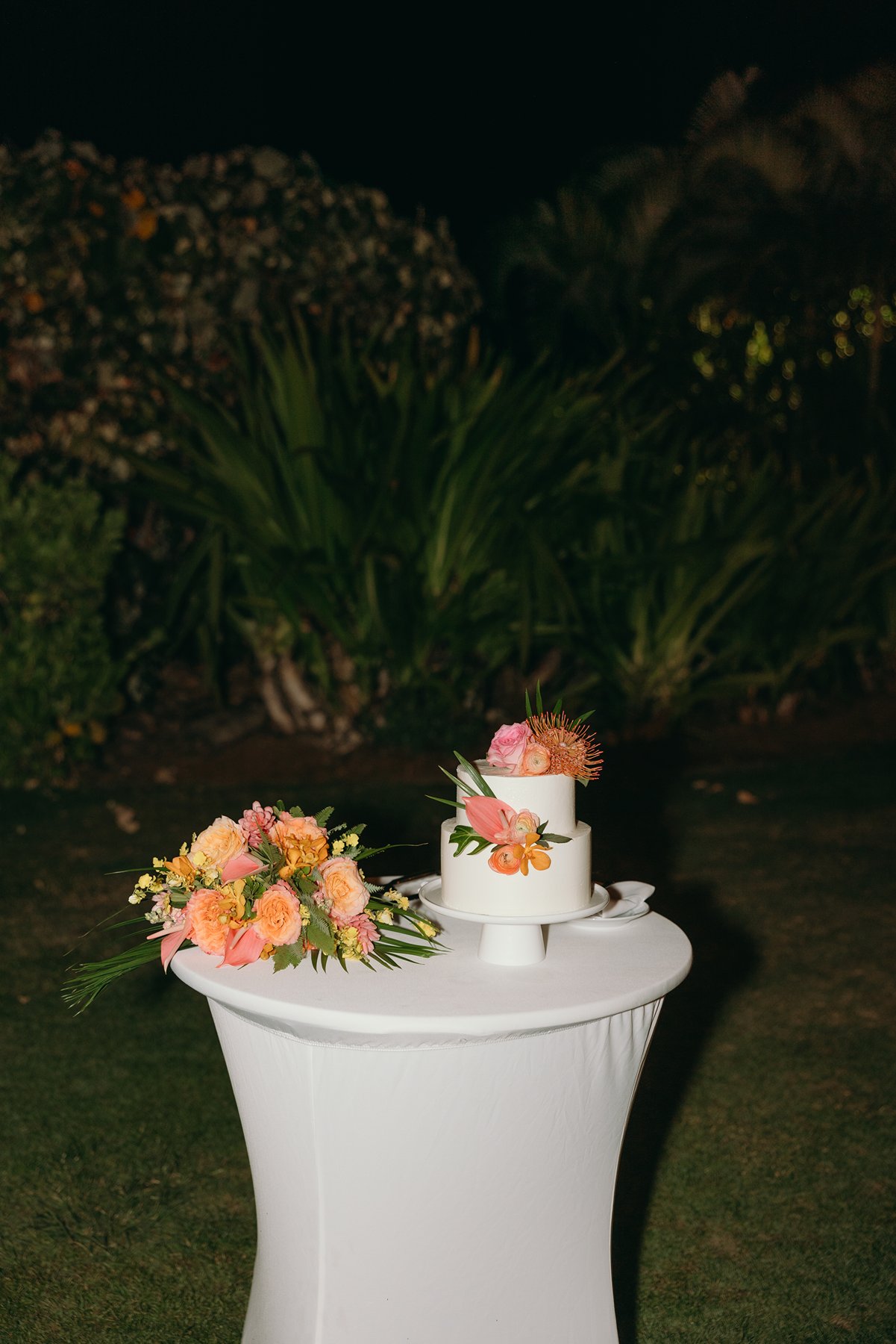 Wedding cake with tropical flowers displayed on table at nighttime outdoor reception