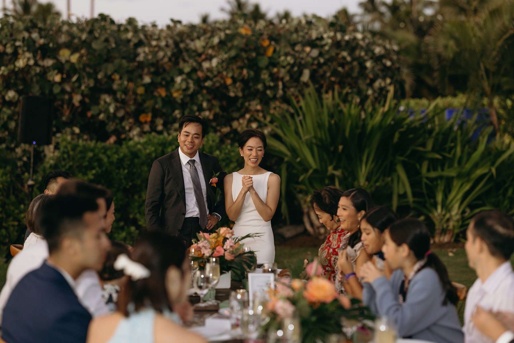 Bride and groom smiling and giving speech to guests during outdoor reception at resort wedding venue