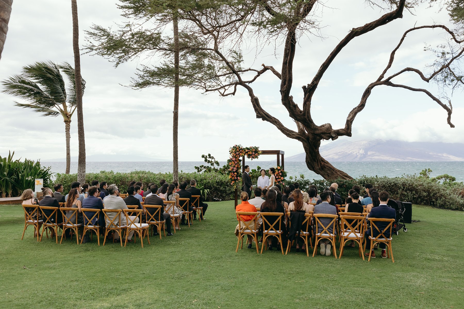 Wide view of outdoor ceremony setup with guests and ocean backdrop at Maui resort wedding venue