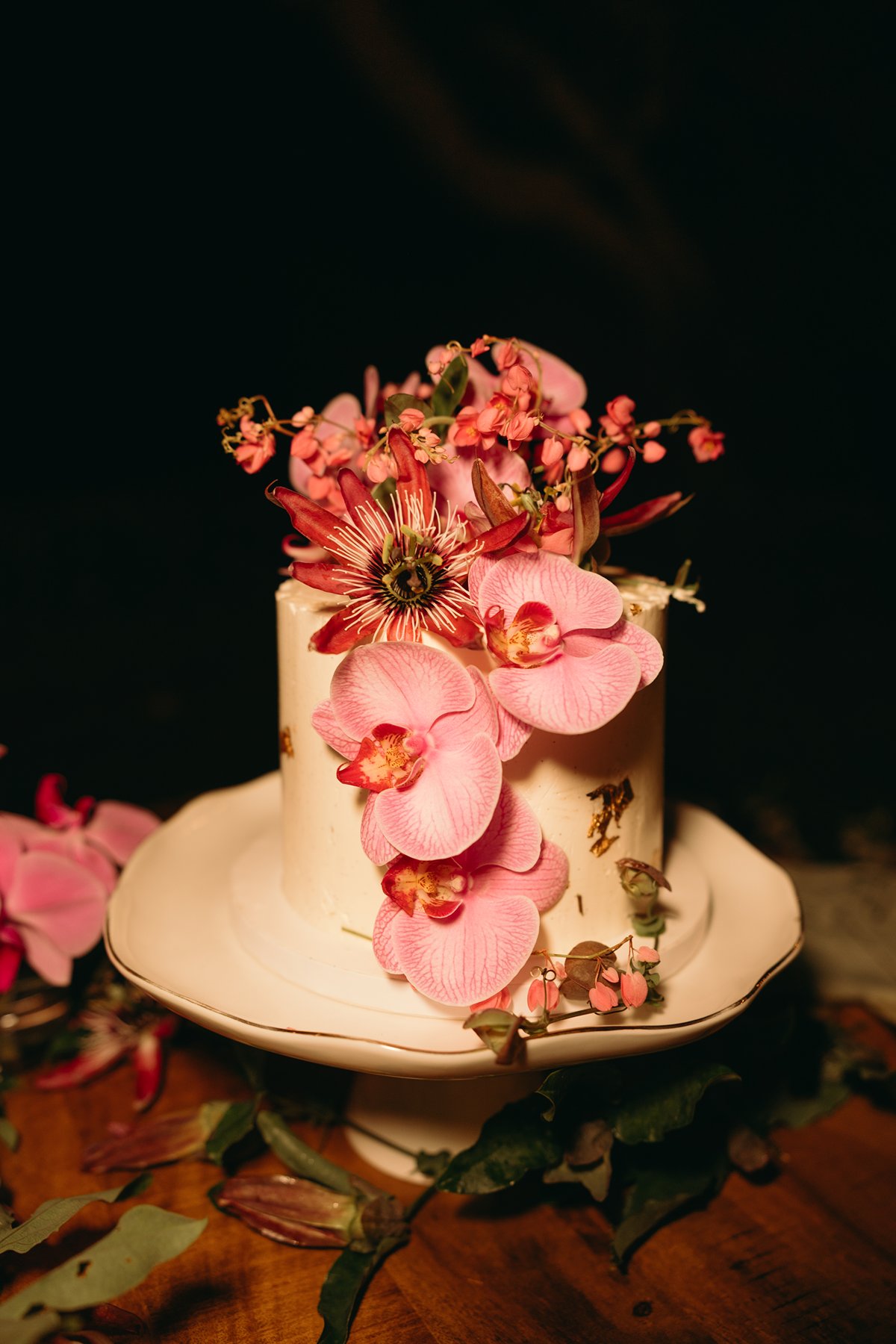 Close-up of a white wedding cake decorated with pink orchids and tropical blooms, styled for an intimate Maui celebration.