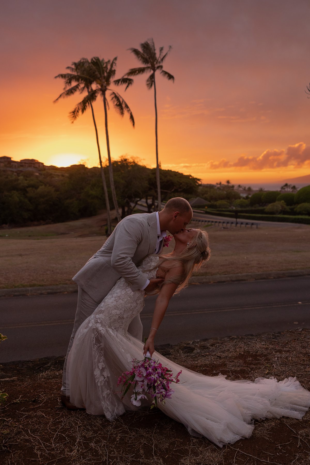 Romantic sunset dip and kiss overlooking the ocean as a couple celebrates their decision to elope in Maui, palm trees silhouetted against an orange sky.