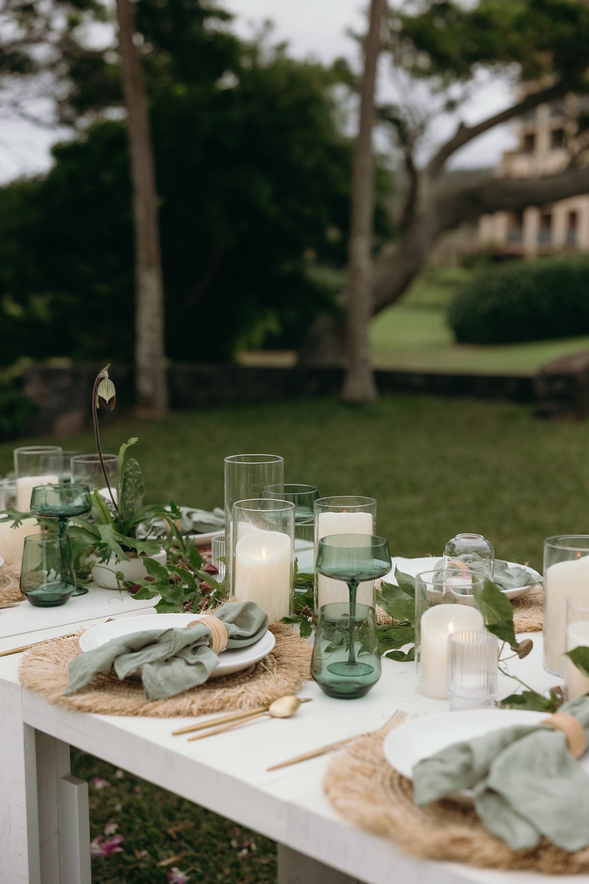 Intimate reception table styled with woven placemats, soft green napkins, and candlelight for a romantic Maui wedding dinner.