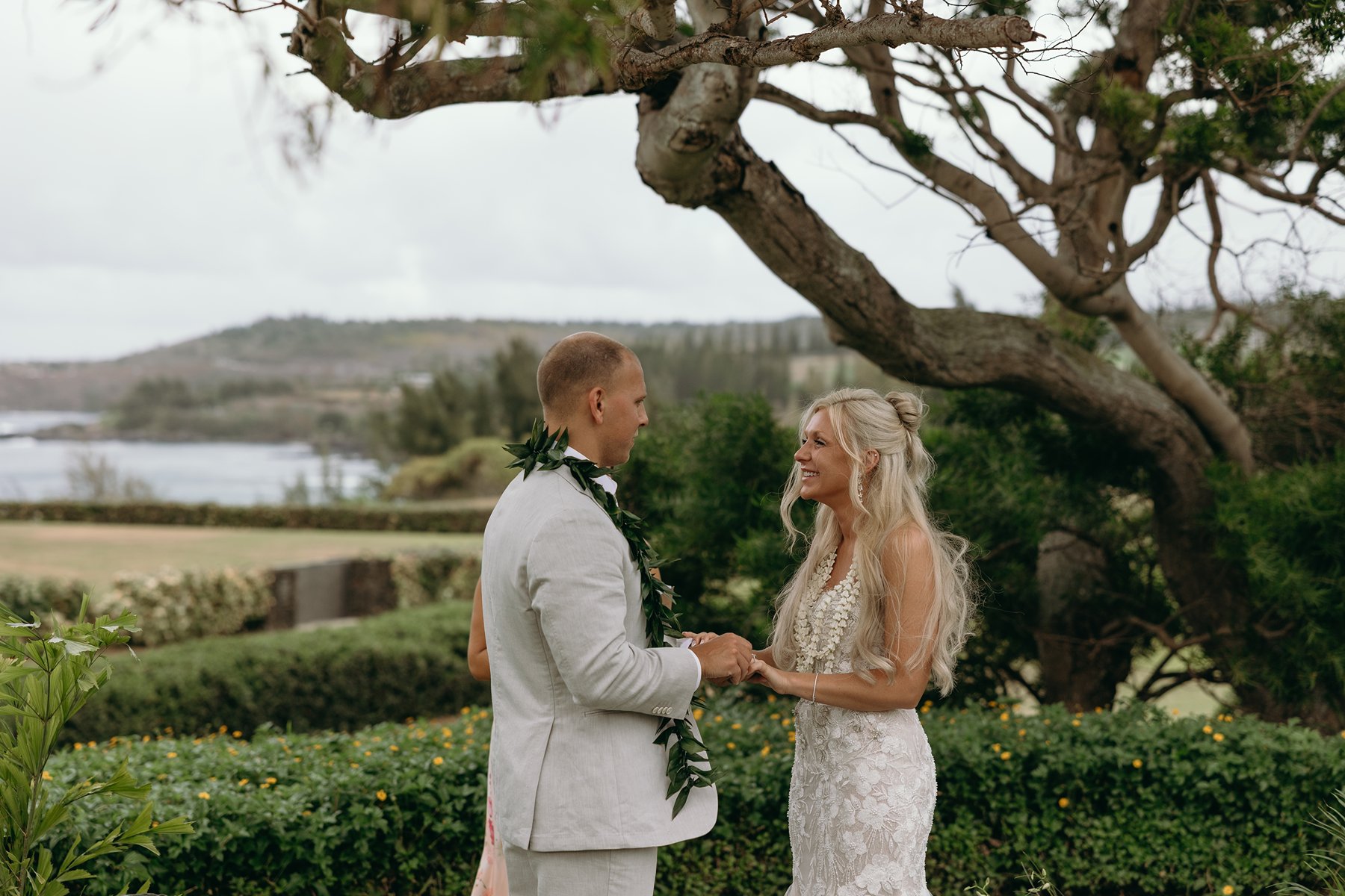 Bride and groom holding hands and smiling during their heartfelt vows as they elope in Maui, lush greenery surrounding them.
