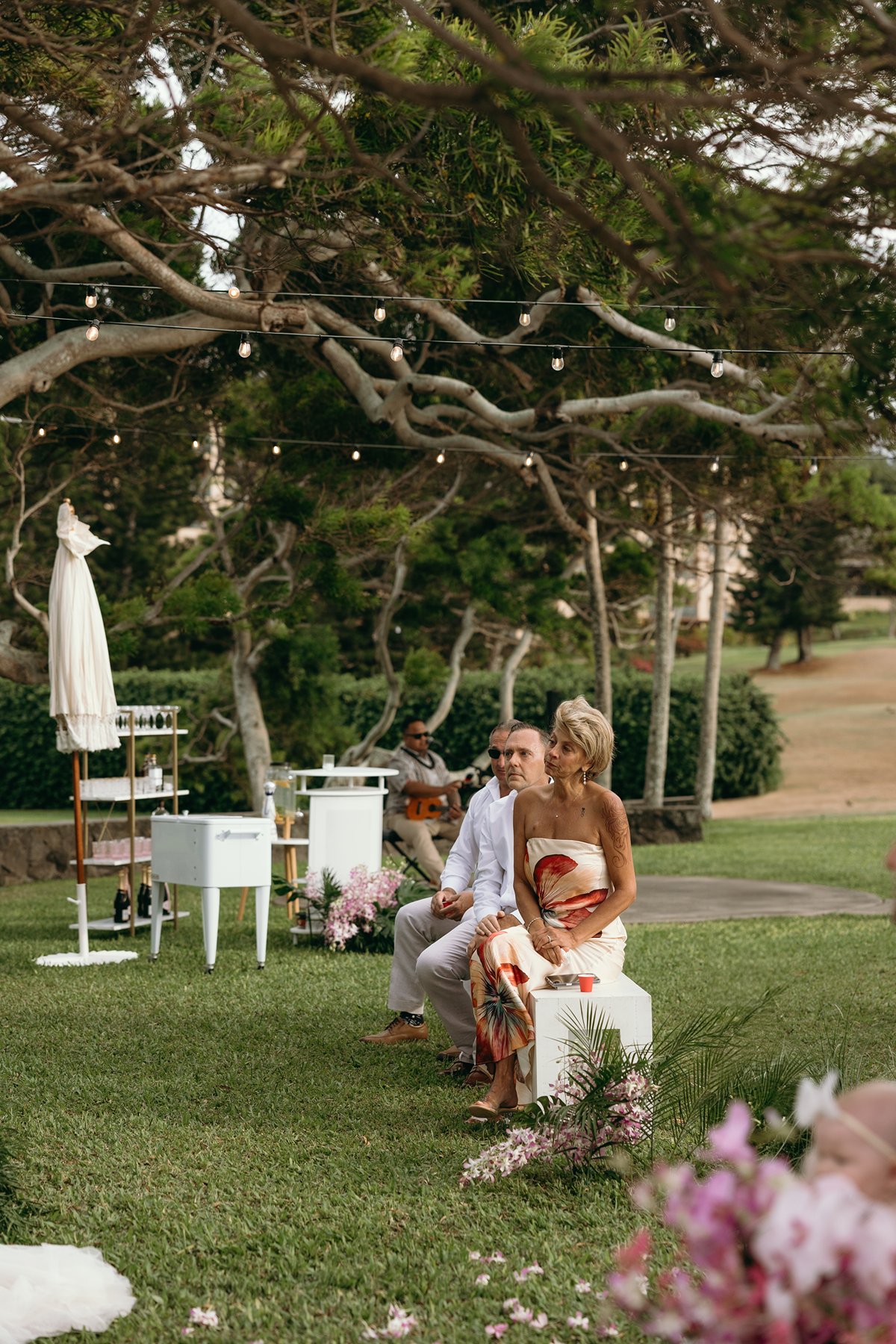 Live musician playing guitar beneath string lights during a garden ceremony after the couple chose to elope in Maui.