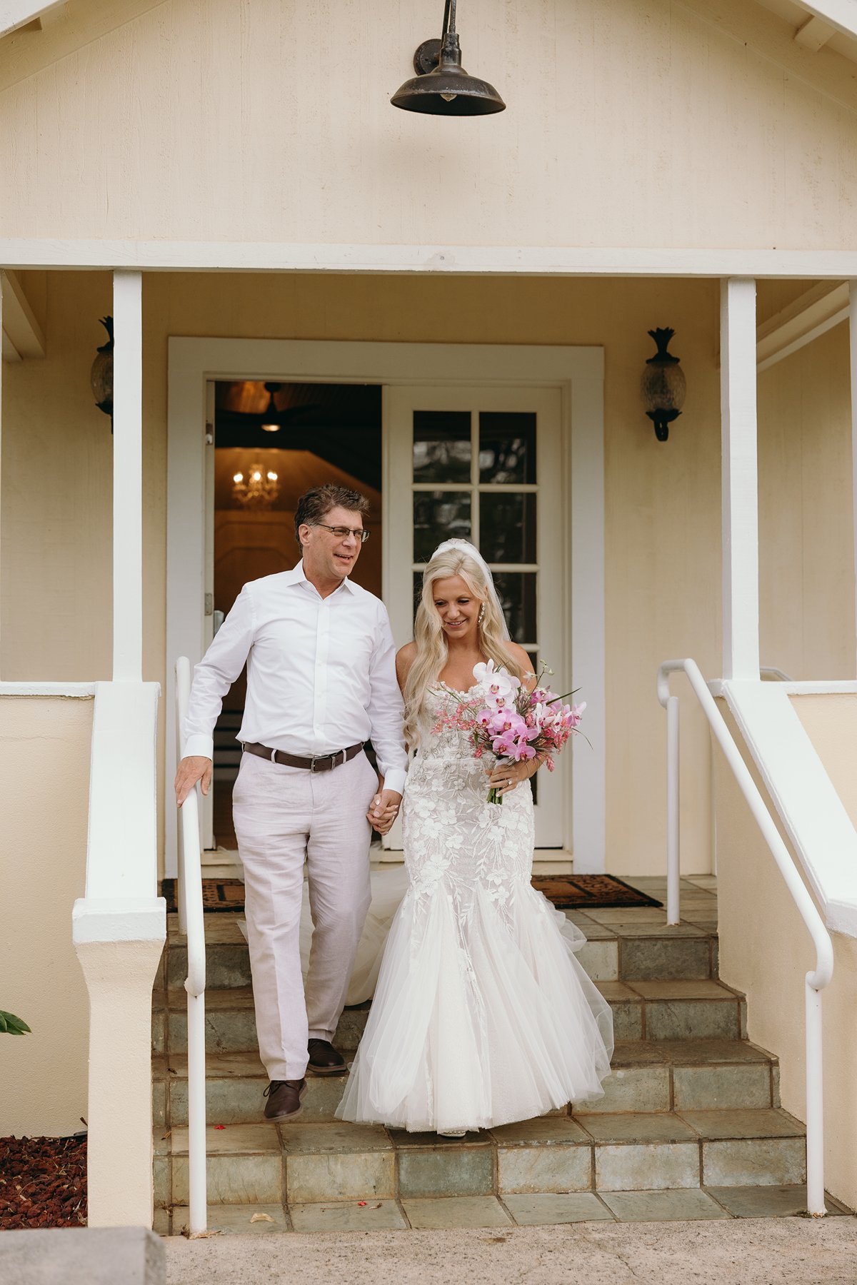 Bride walking down the steps with her father before the ceremony, bouquet of pink orchids in hand.