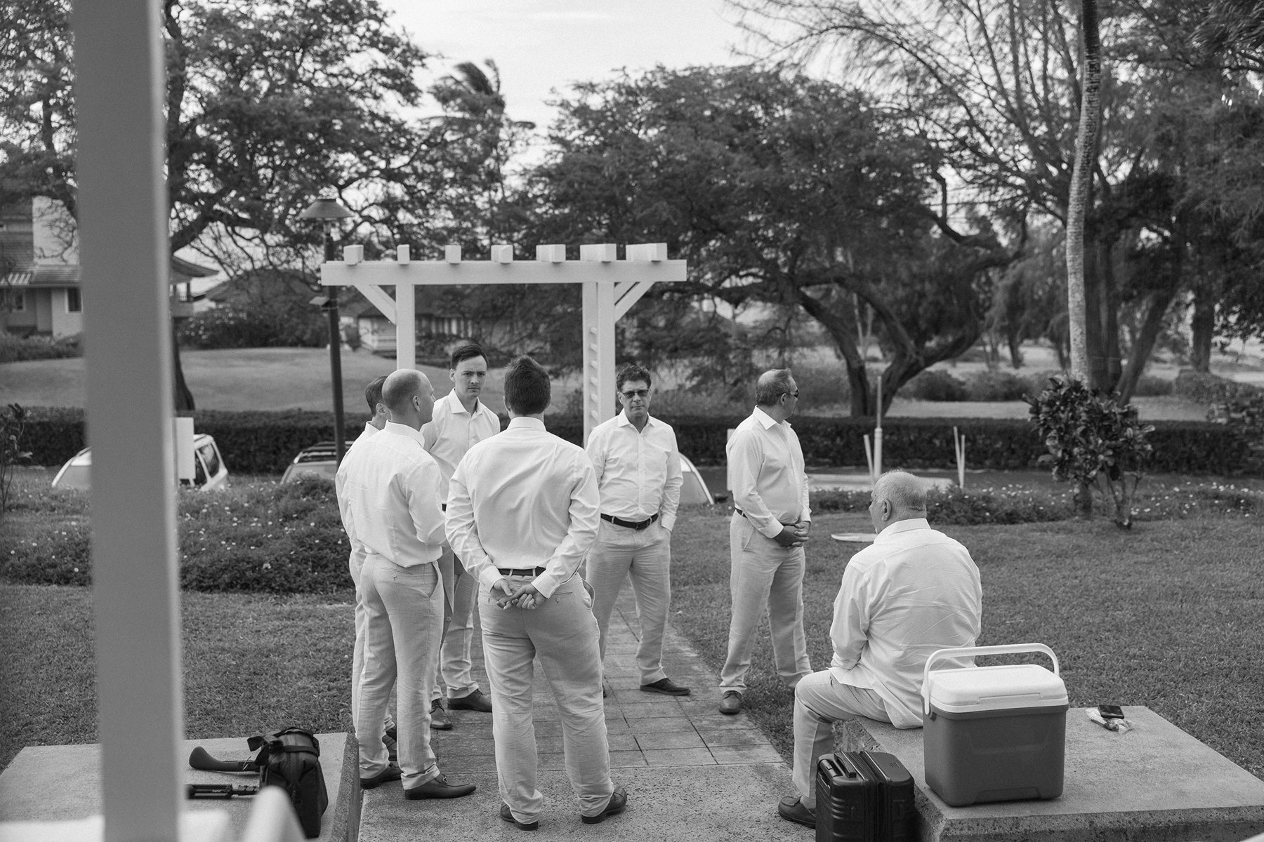 Groomsmen gathered on the lawn before the ceremony, chatting beneath island trees ahead of their friends choosing to elope in Maui.