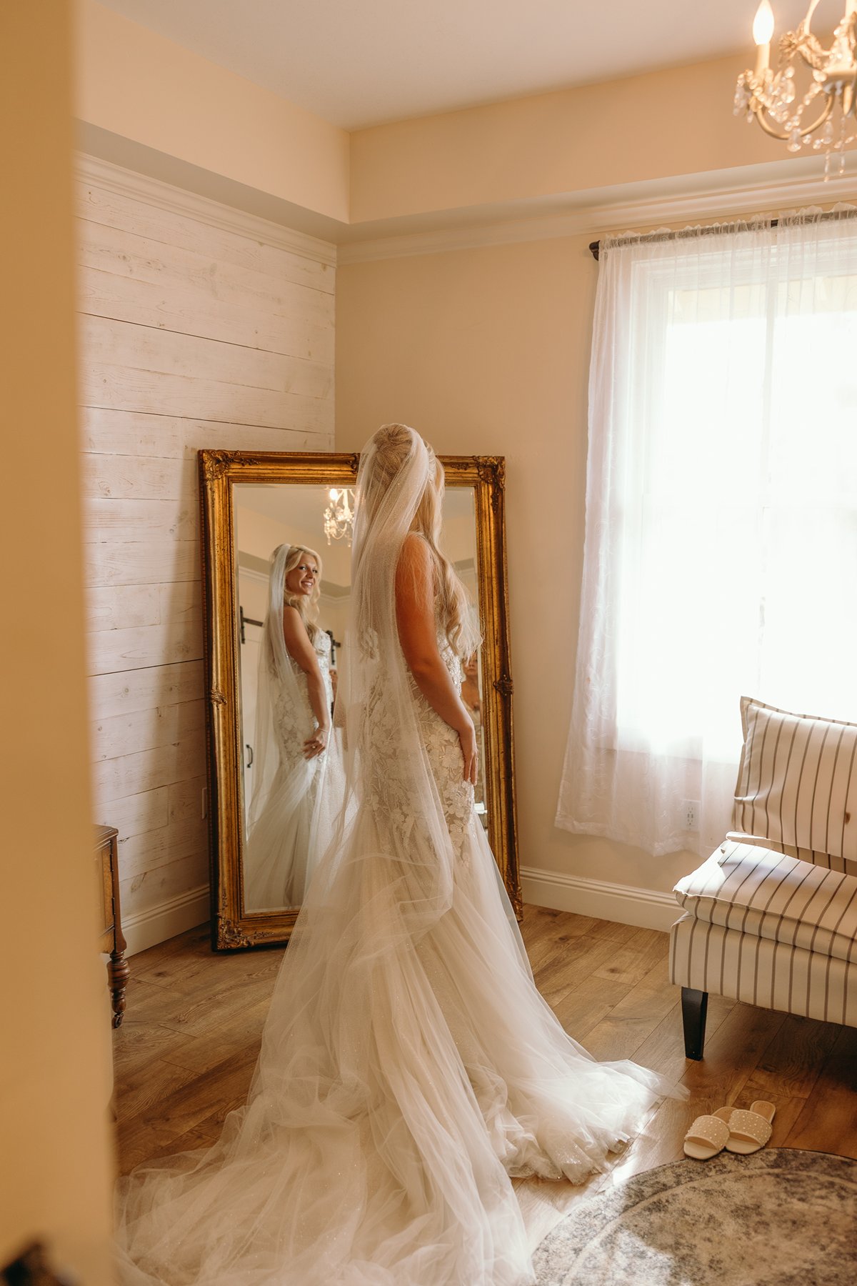 Bride admiring her lace wedding gown in a gold-framed mirror, getting ready for her Hawaii elopement ceremony.