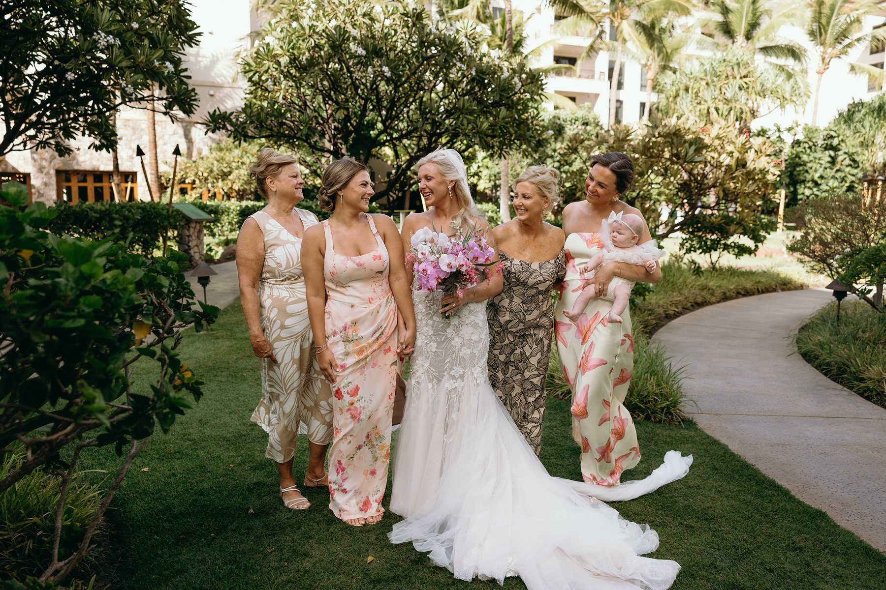 Bride laughing with her bridesmaids in a lush resort garden after deciding to elope in Maui, tropical florals bright against soft greenery.