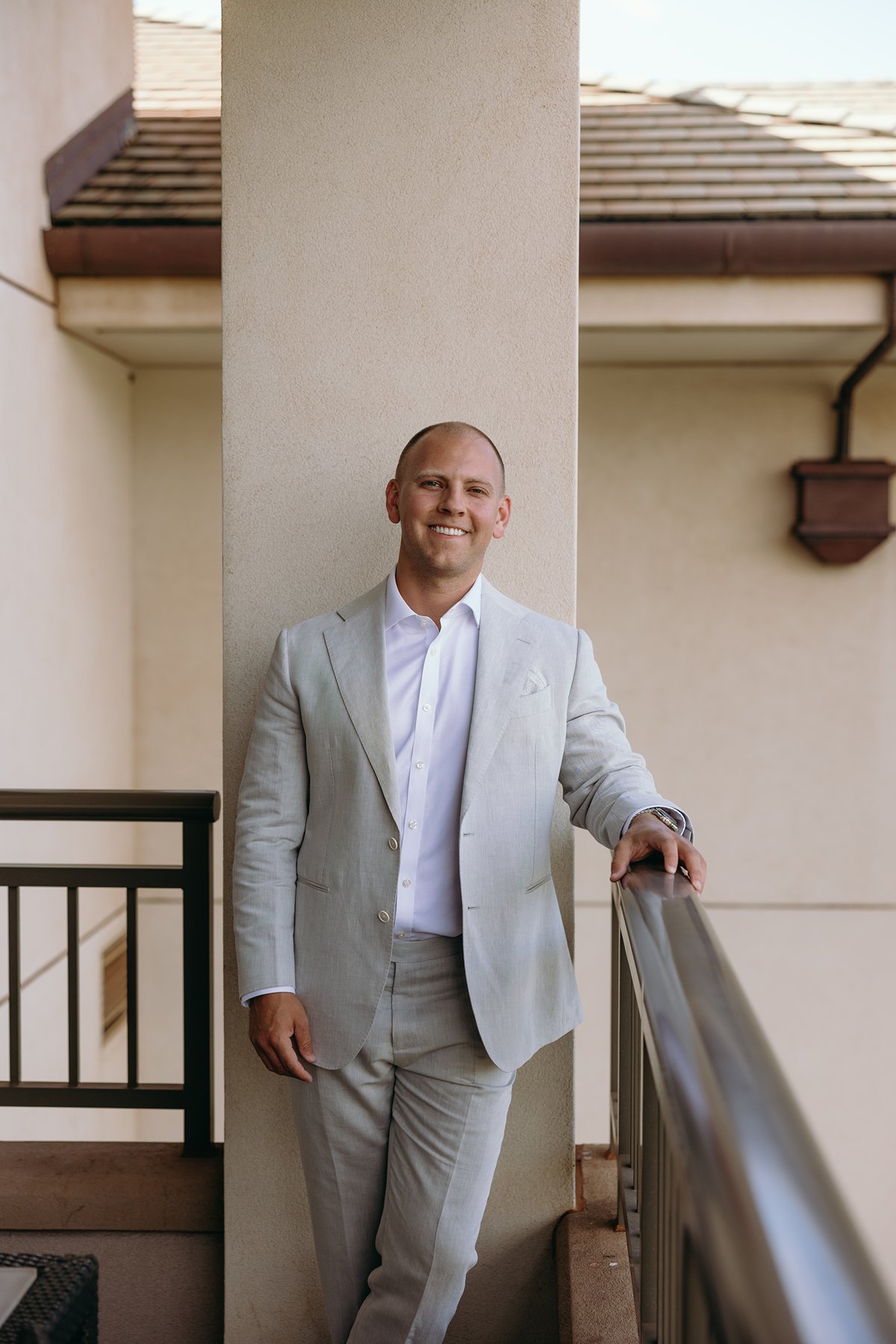 Groom smiling on a resort balcony in a light gray suit as he prepares to elope in Maui.