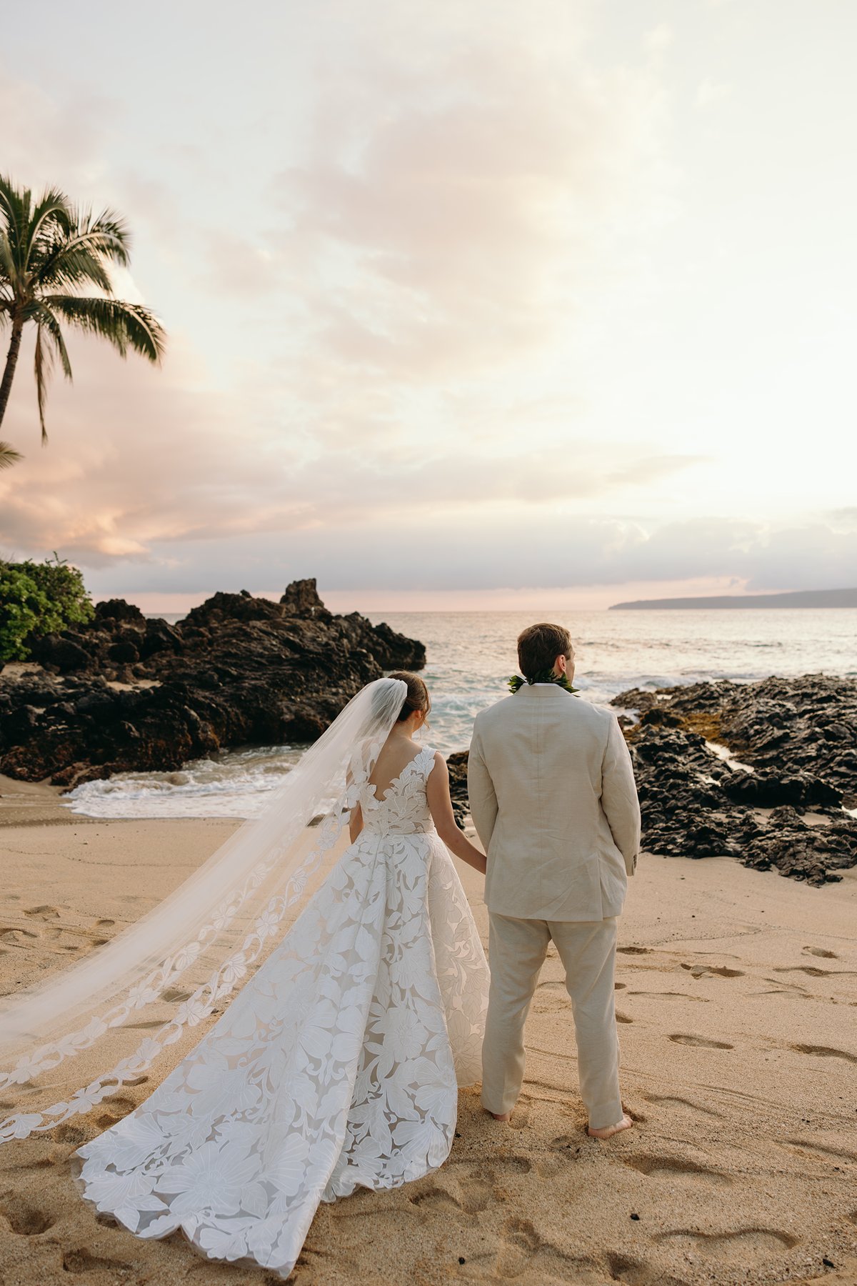 Newlywed couple standing on a secluded Maui shoreline with volcanic rock formations and pastel sunset sky during elopement photography.