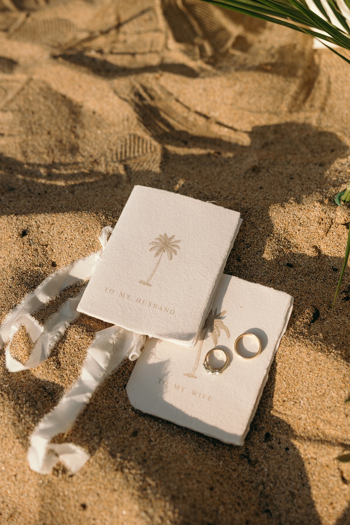 Hawaii marriage license booklet and wedding rings placed in the sand with tropical shadows during a Maui elopement photography detail shot.