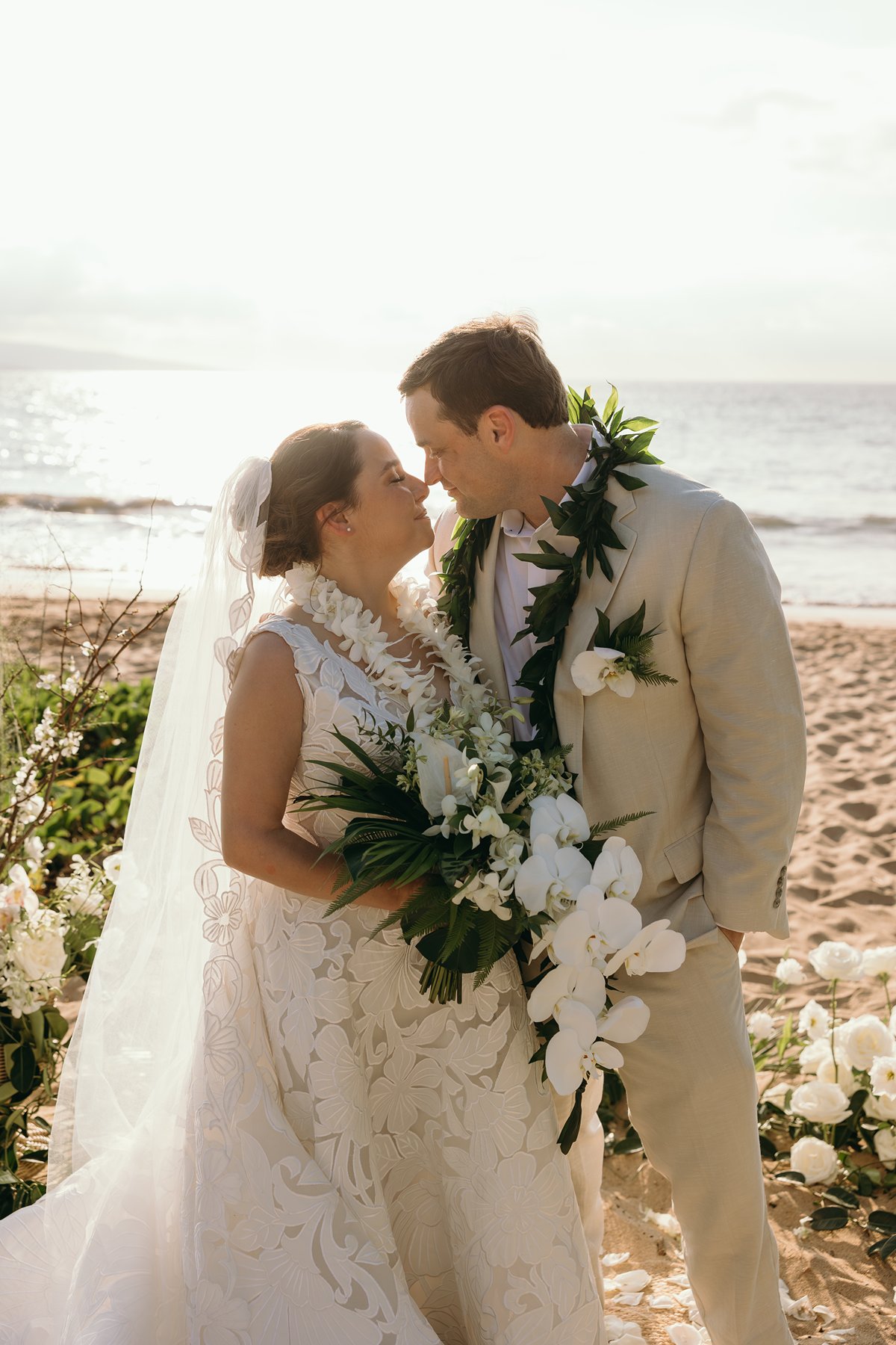 Newlywed couple smiling at each other on a Maui beach while wearing traditional Hawaiian leis during their elopement photography session.