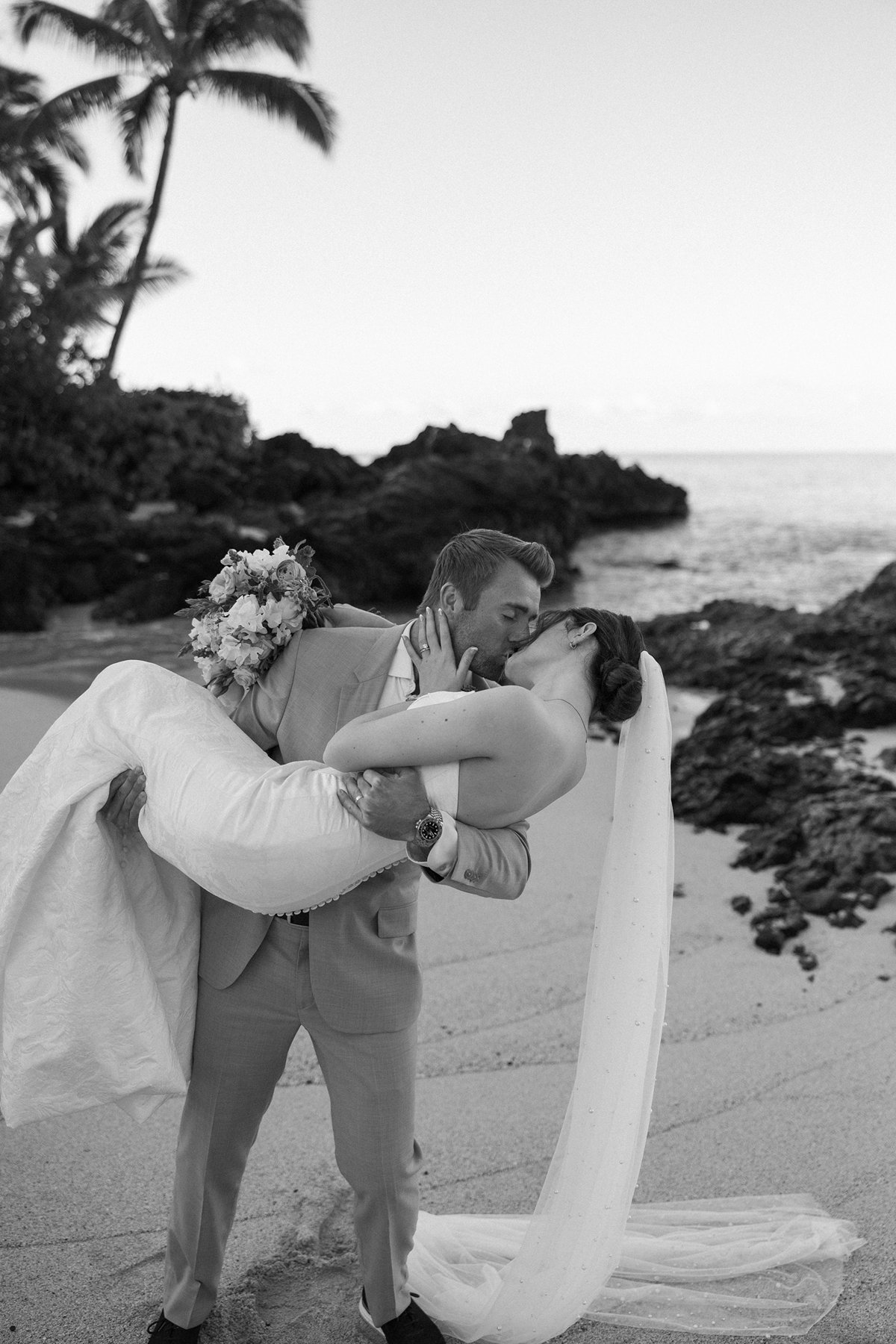 Black and white sneak peek photos of groom dipping bride for a kiss by the ocean