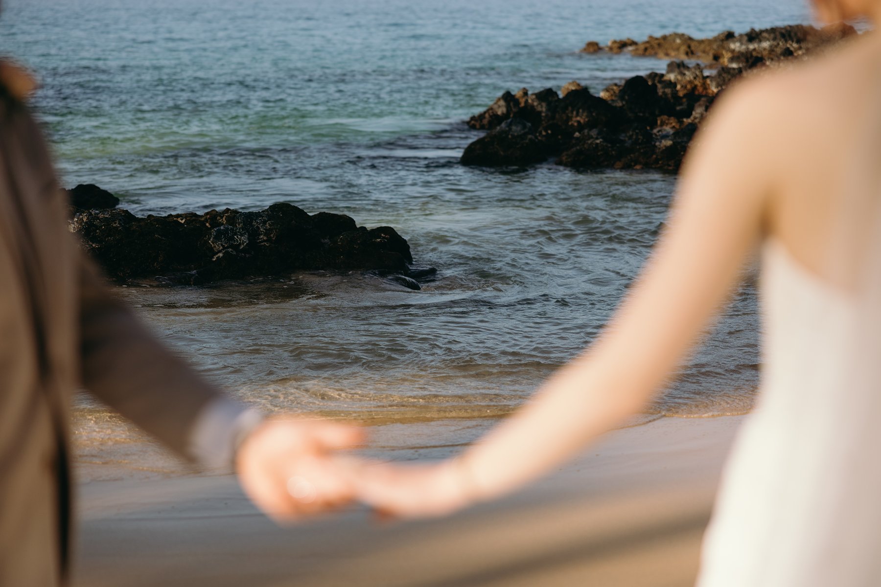 Artistic blurred foreground of couple holding hands by the ocean in creative sneak peek photos