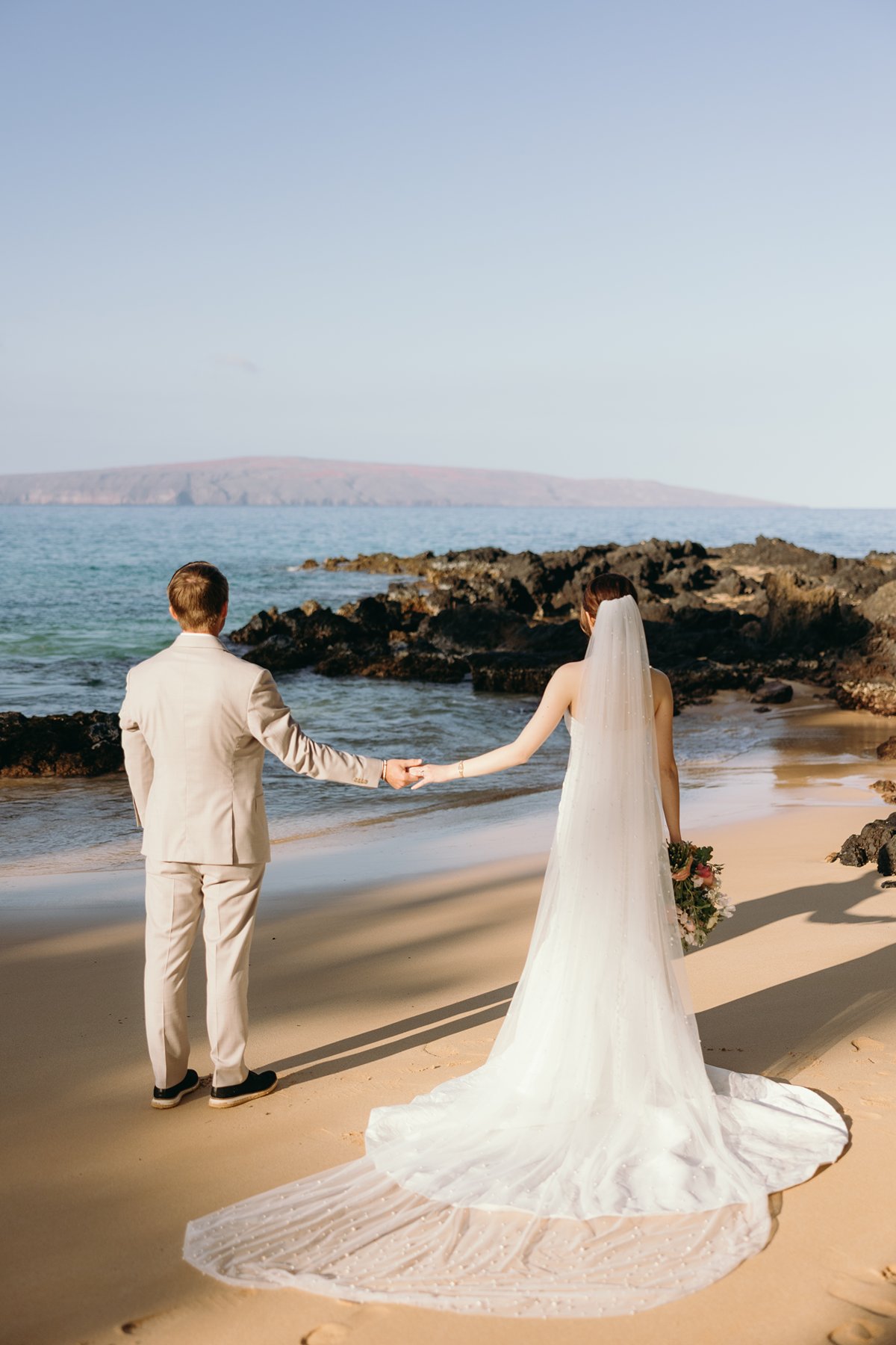 Bride and groom holding hands while walking along shoreline in Maui wedding sneak peek photos