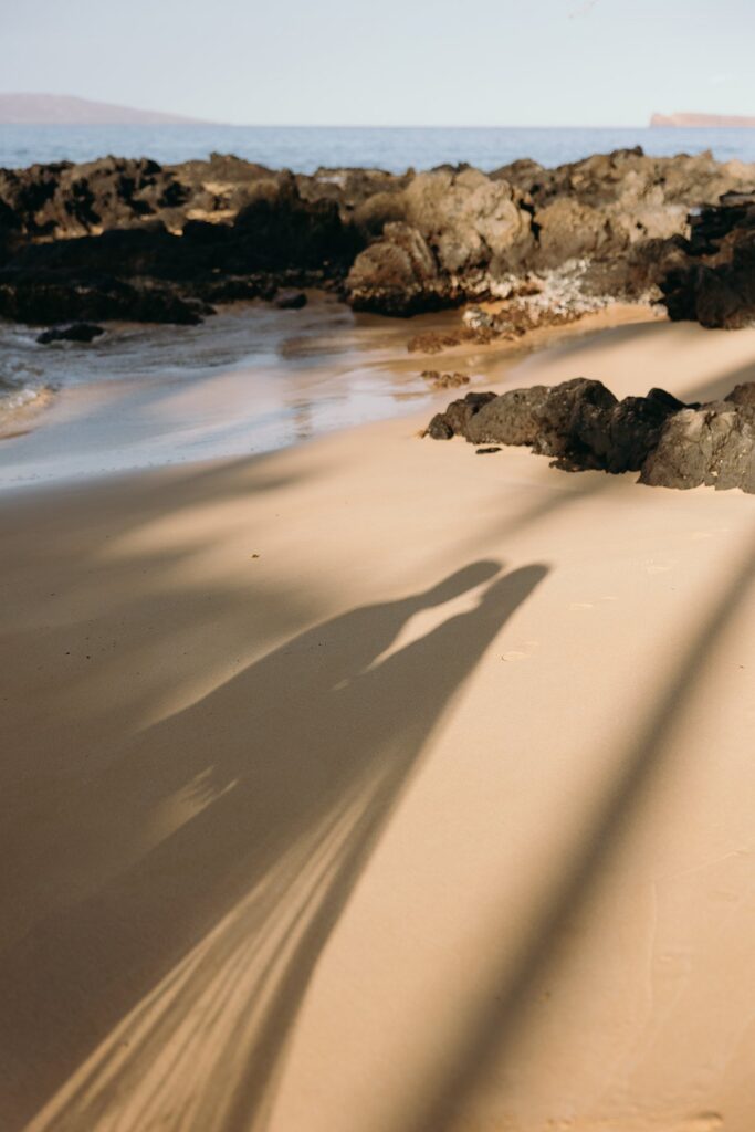 Romantic shadow of couple cast on sandy beach at sunset in artistic wedding sneak peek photos