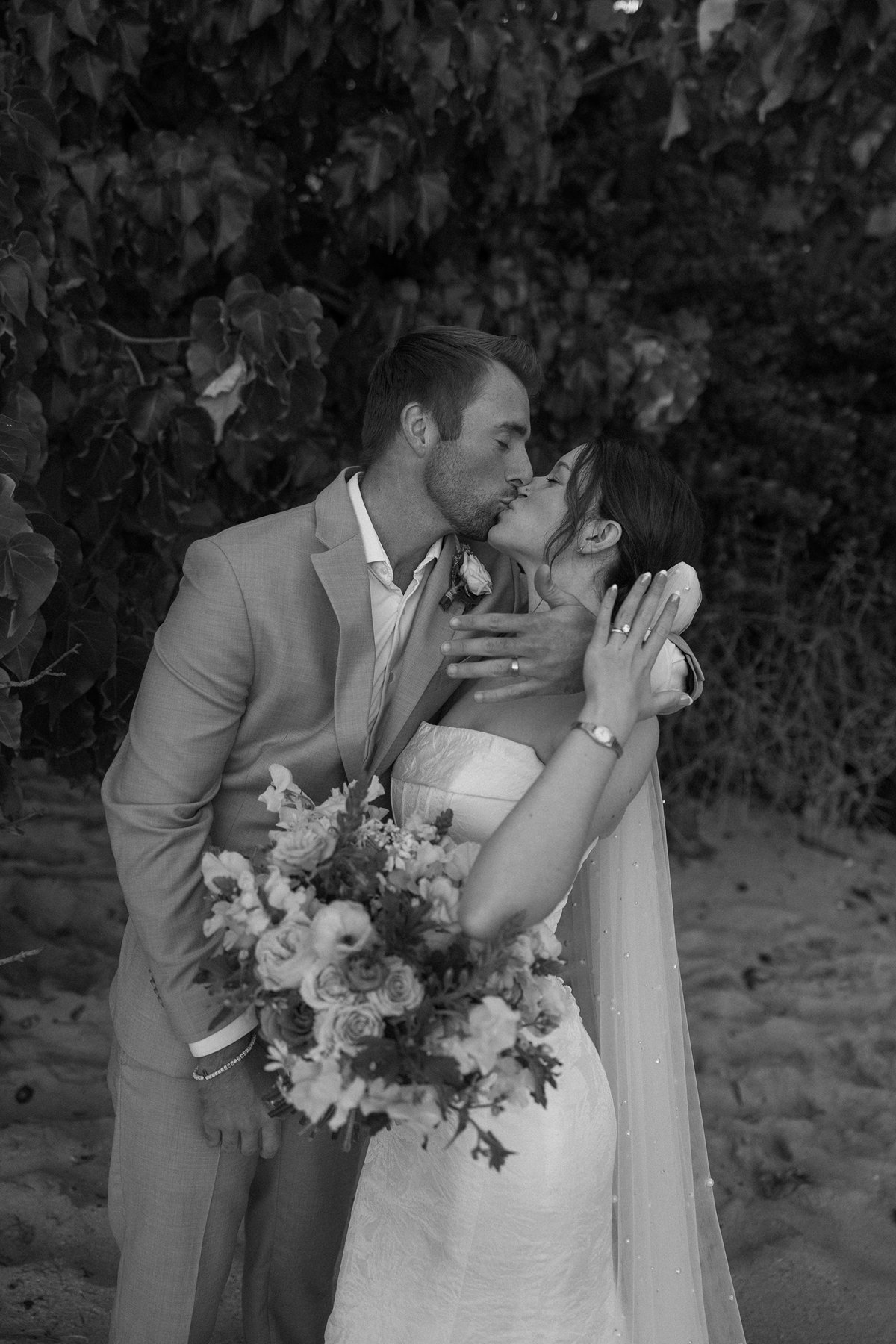 Black and white portrait of bride and groom kissing with bouquet in romantic sneak peek photos