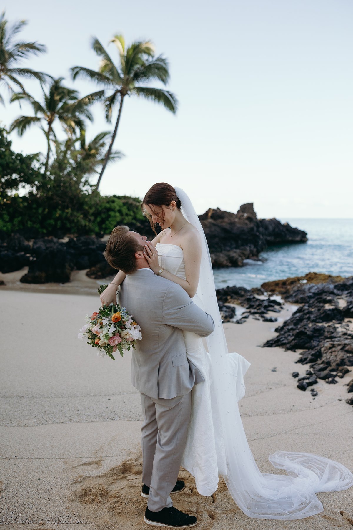 Groom lifting bride in a playful embrace on sandy beach in candid sneak peek photos