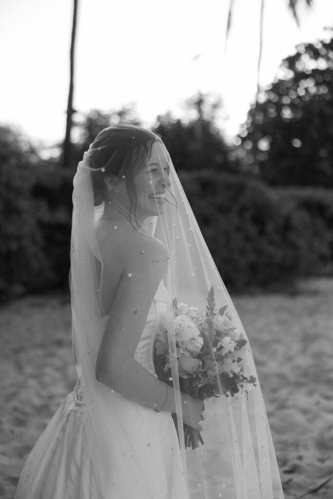 Soft black and white portrait of smiling bride in veil holding bouquet during sneak peek photos