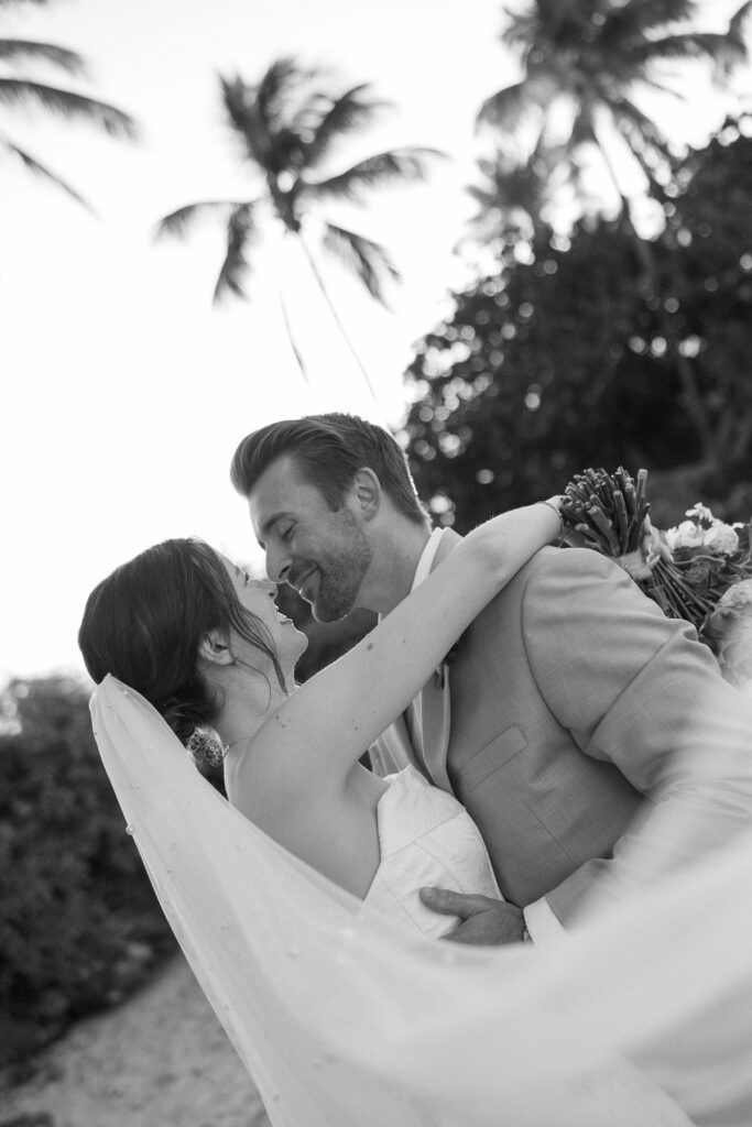Intimate black and white sneak peek photos of bride and groom embracing under palm trees