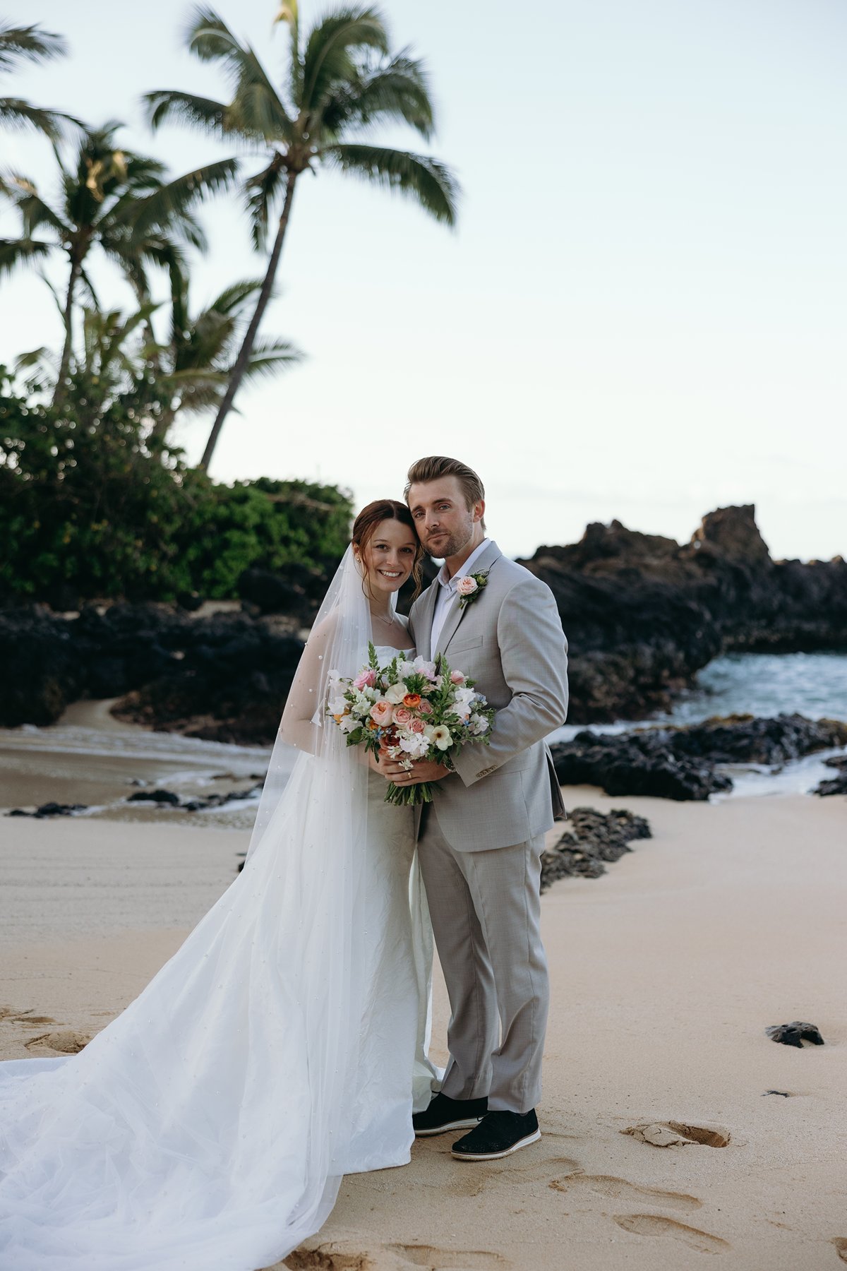 Newlyweds posing together with bouquet on a Maui beach in wedding sneak peek photos