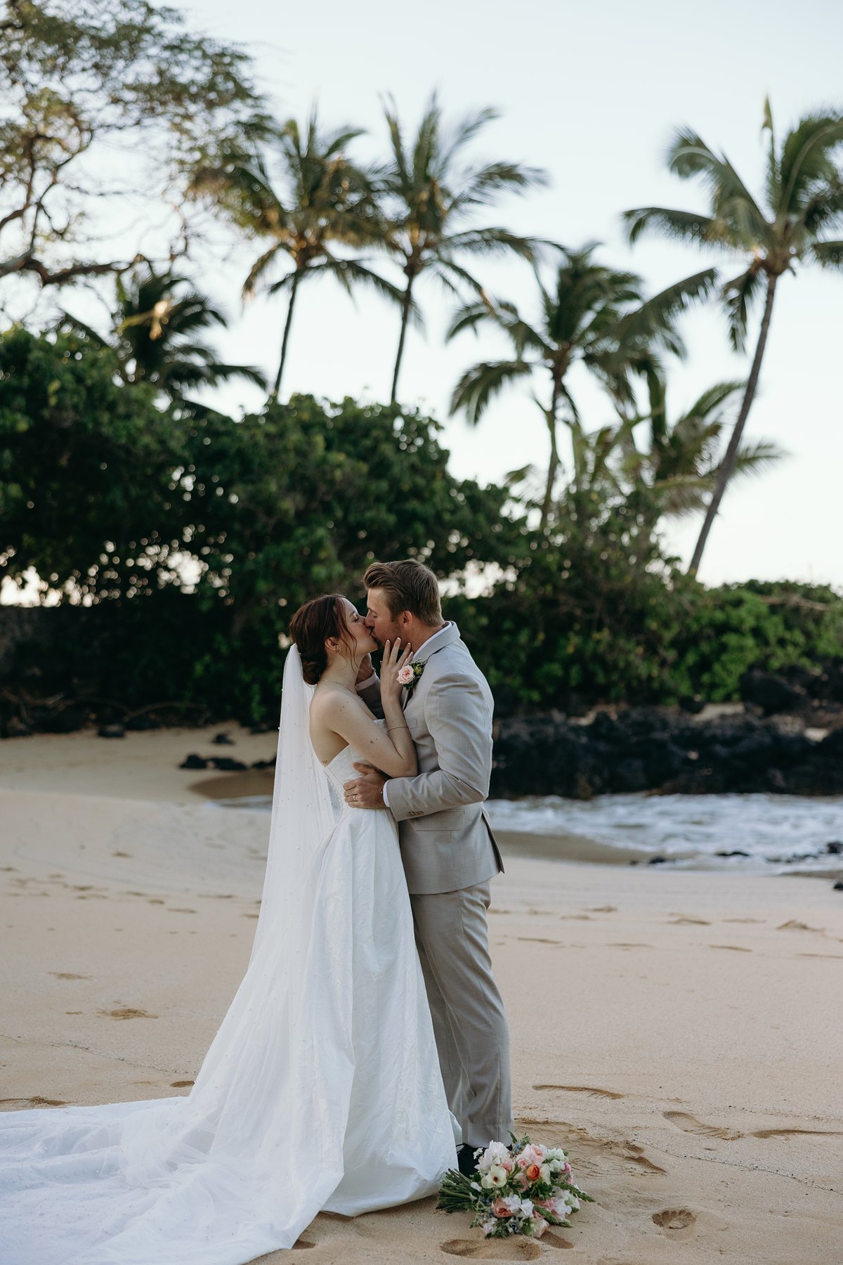 Intimate kiss between bride and groom with ocean waves behind them in sneak peek photos