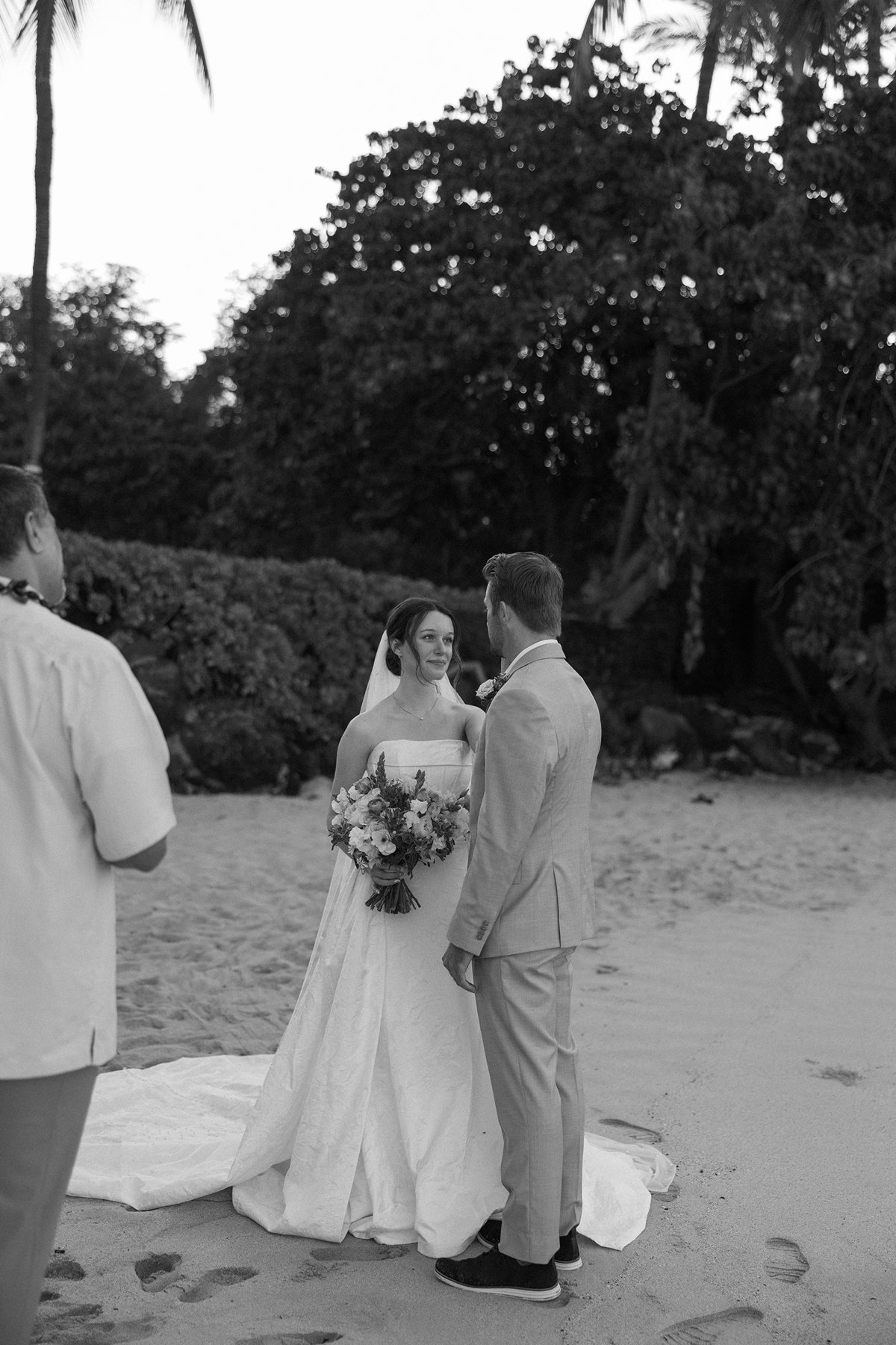 Black and white sneak peek photos of bride and groom exchanging vows on the beach