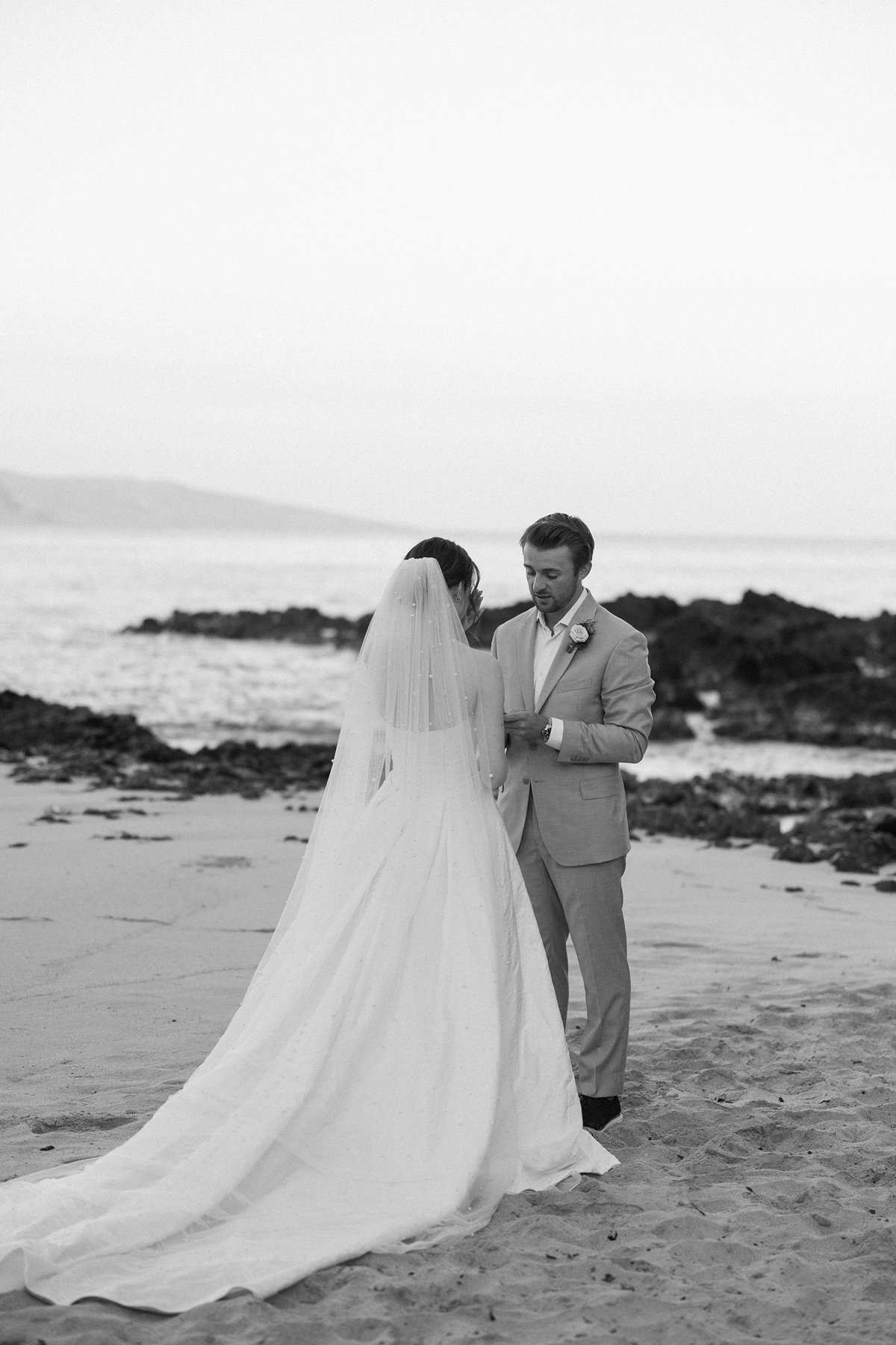 Black and white portrait of bride and groom during vows by the ocean in sneak peek photos