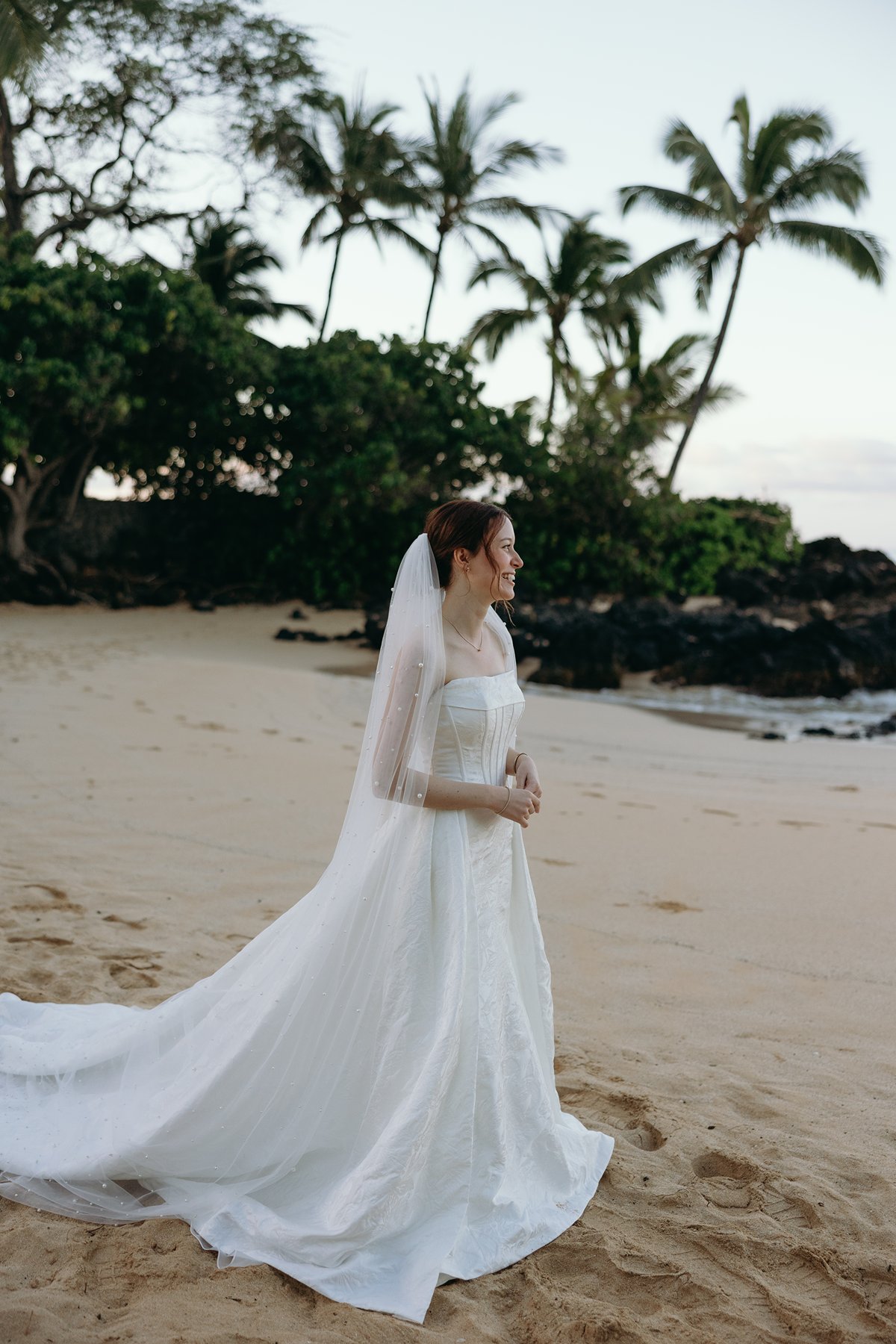 Bride walking along sandy beach in elegant gown and veil during wedding sneak peek photos