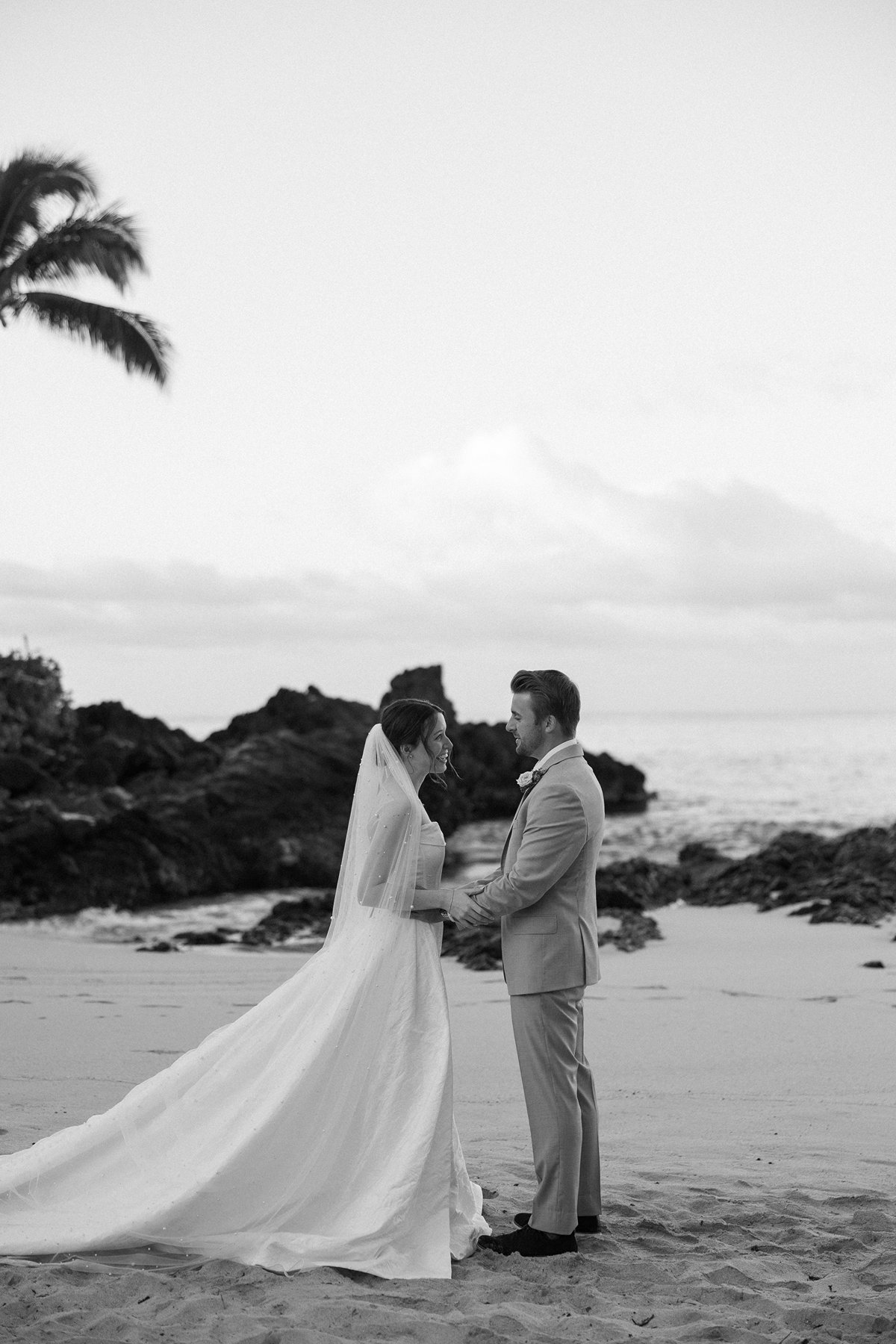 Romantic black and white portrait of newlyweds holding hands by the ocean in sneak peek photos
