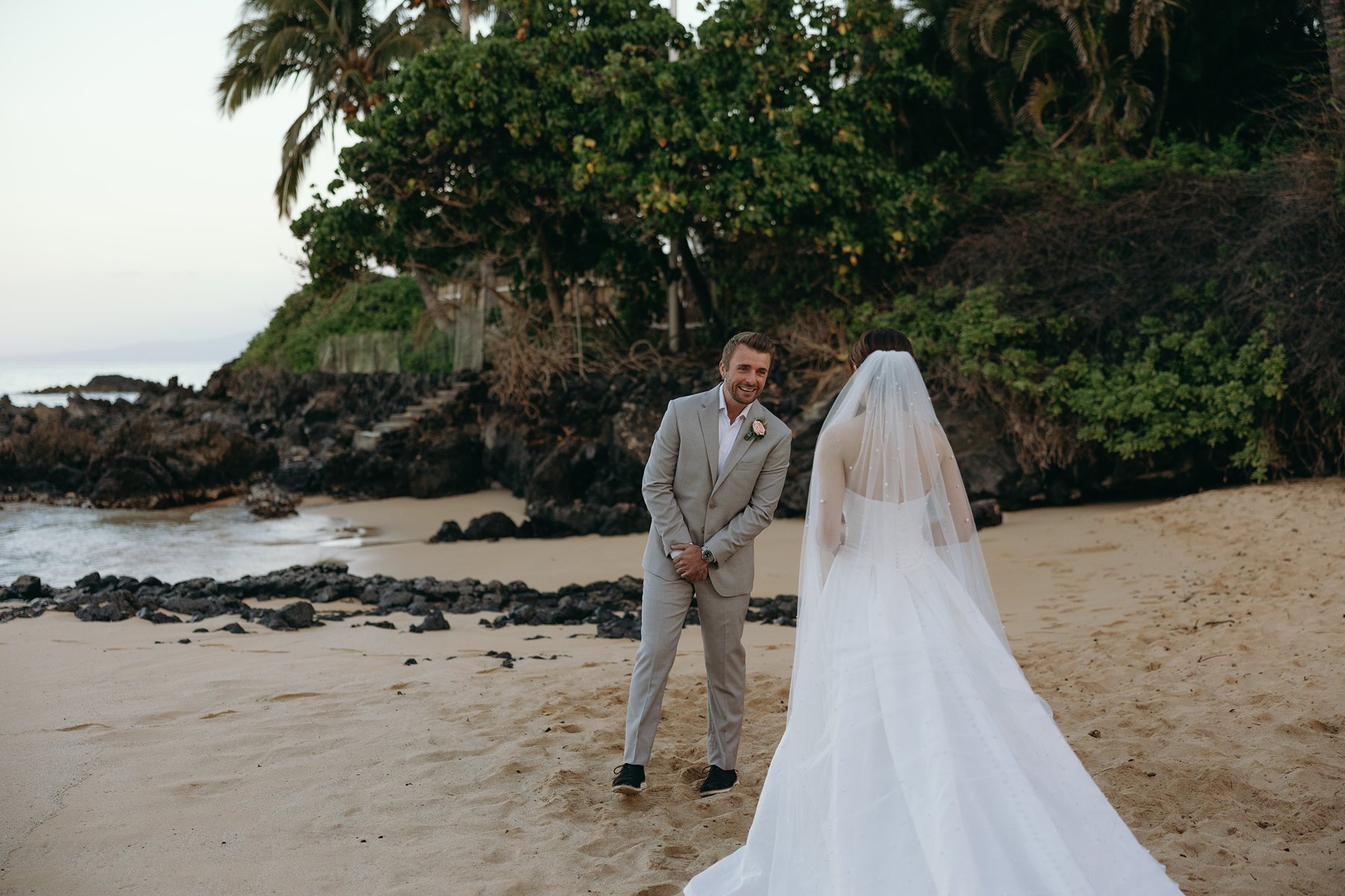 Groom smiling at bride during playful moment on sandy beach in candid wedding sneak peek photos