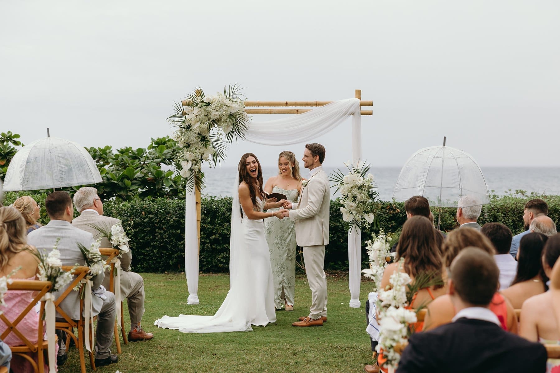 Bride sits on the sand with a vibrant tropical bouquet as ocean waves roll in behind her after her Maui elopement ceremony.
