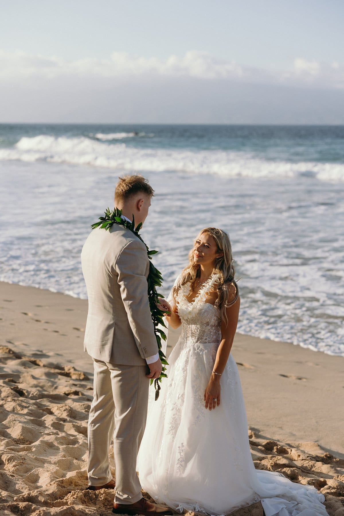 Bride smiles at her partner as they hold hands on a quiet beach during one of their unforgettable Maui elopements.