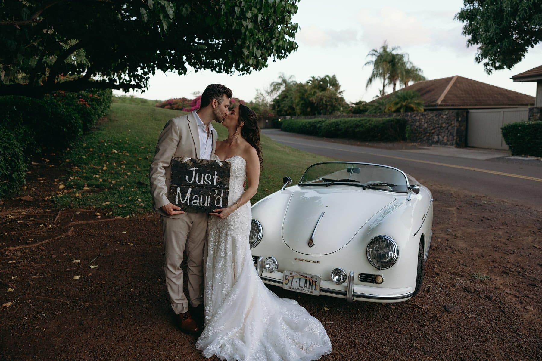Bride and groom kissing beside a vintage convertible with a “Just Maui’d” sign after their Maui elopement