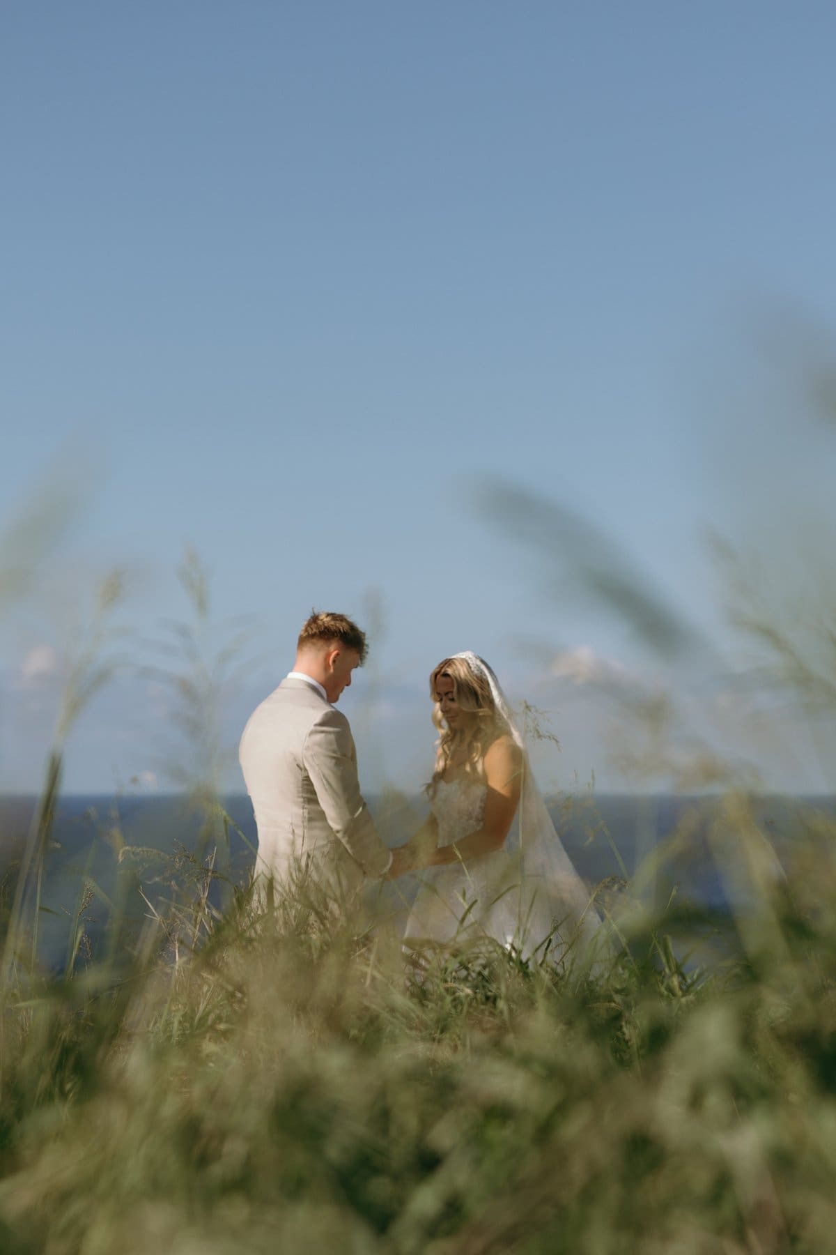 Bride and groom stand together in tall grass with sweeping ocean views during their intimate Maui elopement ceremony.