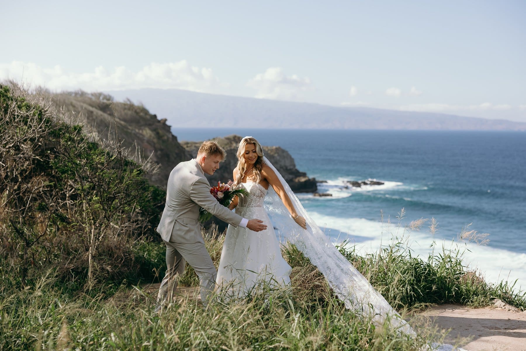 Groom helping arrange the bride's veil during portraits above the ocean after their Maui elopement